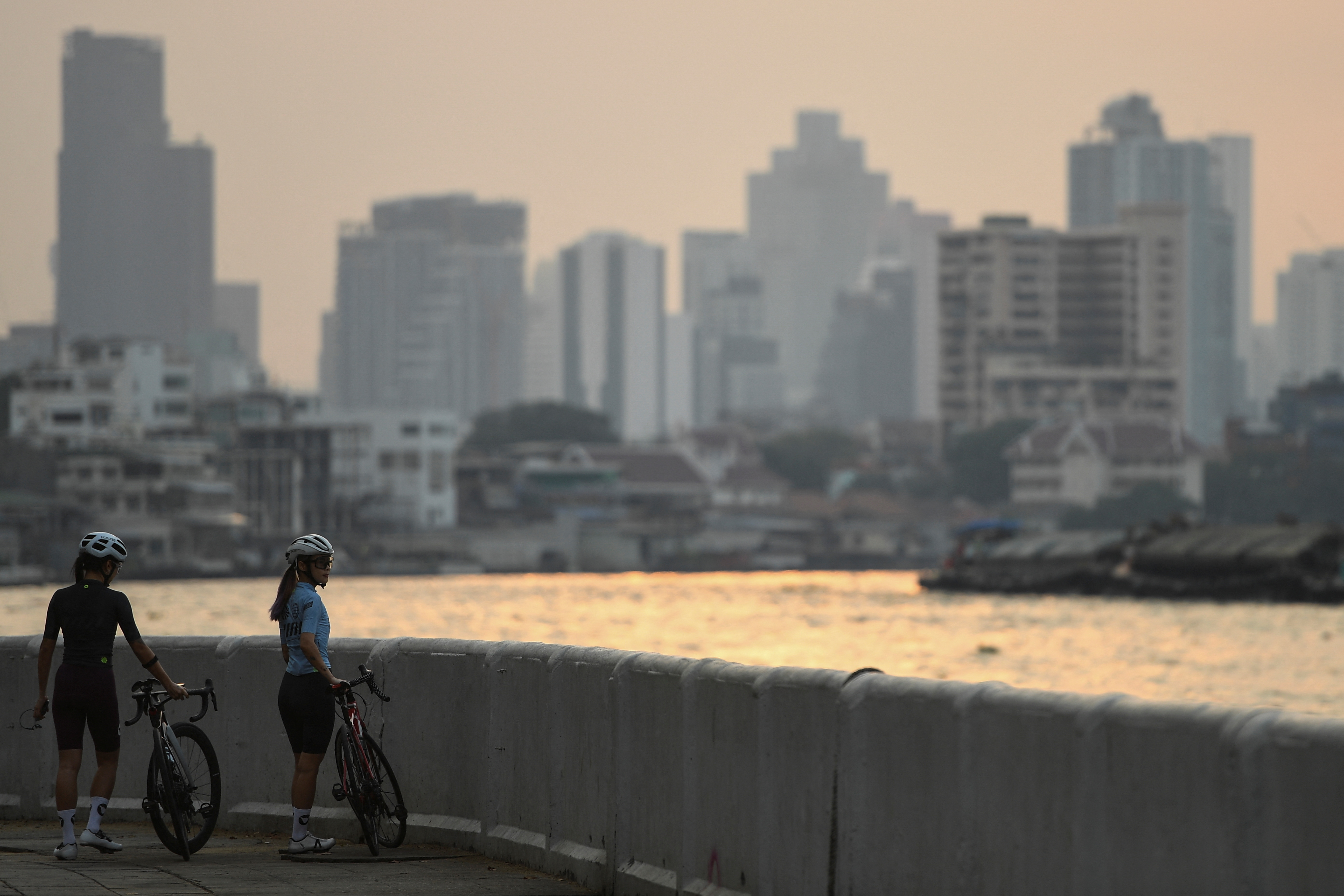 Women with bicycles stand by the Chao Phraya River amid air pollution in Bangkok