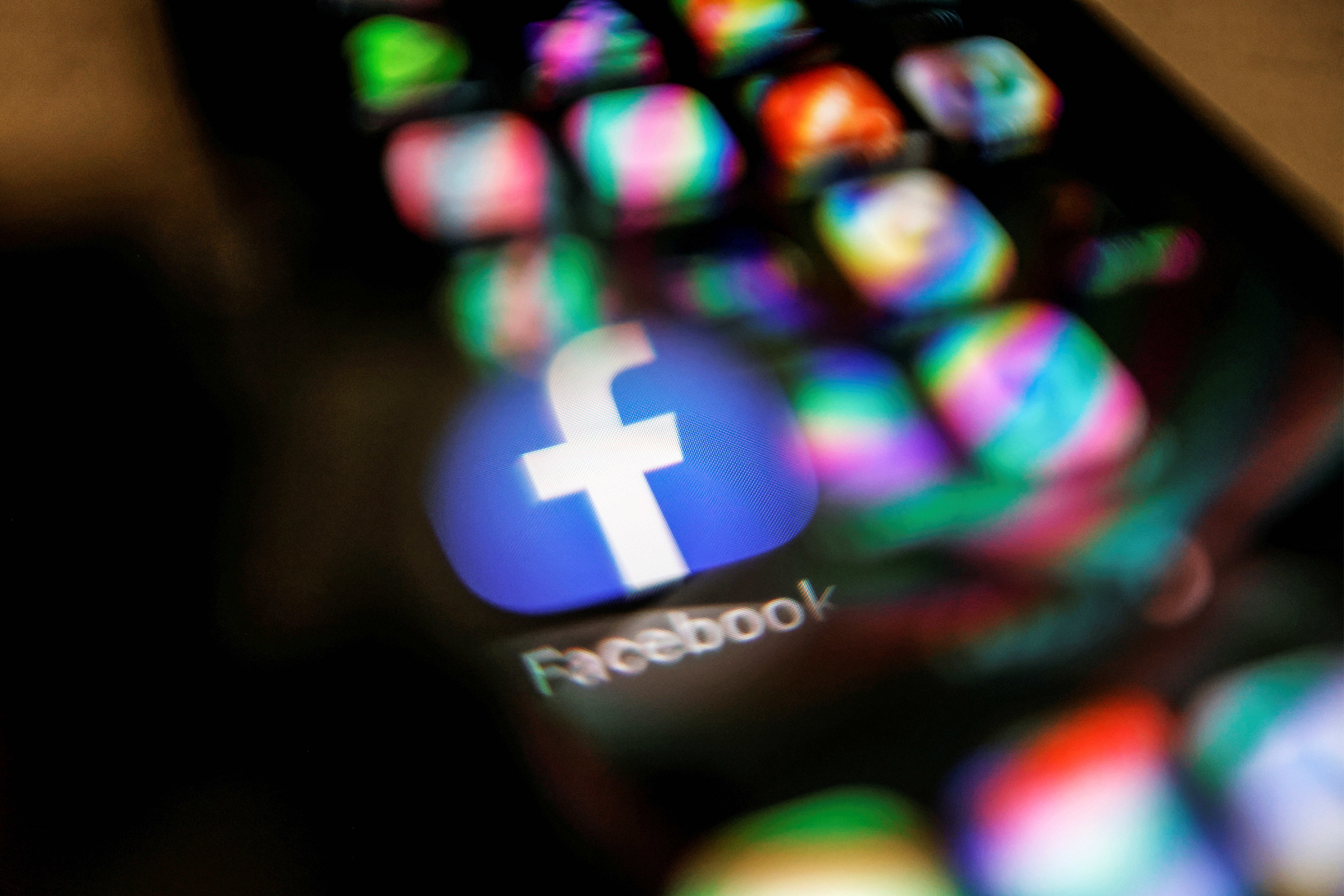 Facebook logo displayed on a mobile phone is seen through a magnifying glass in this picture illustration