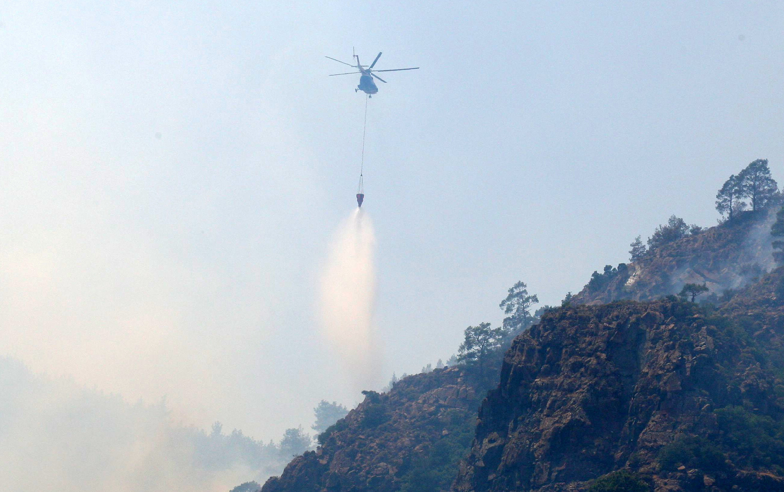 A firefighting helicopter drops water to extinguish a wildfire near Marmaris