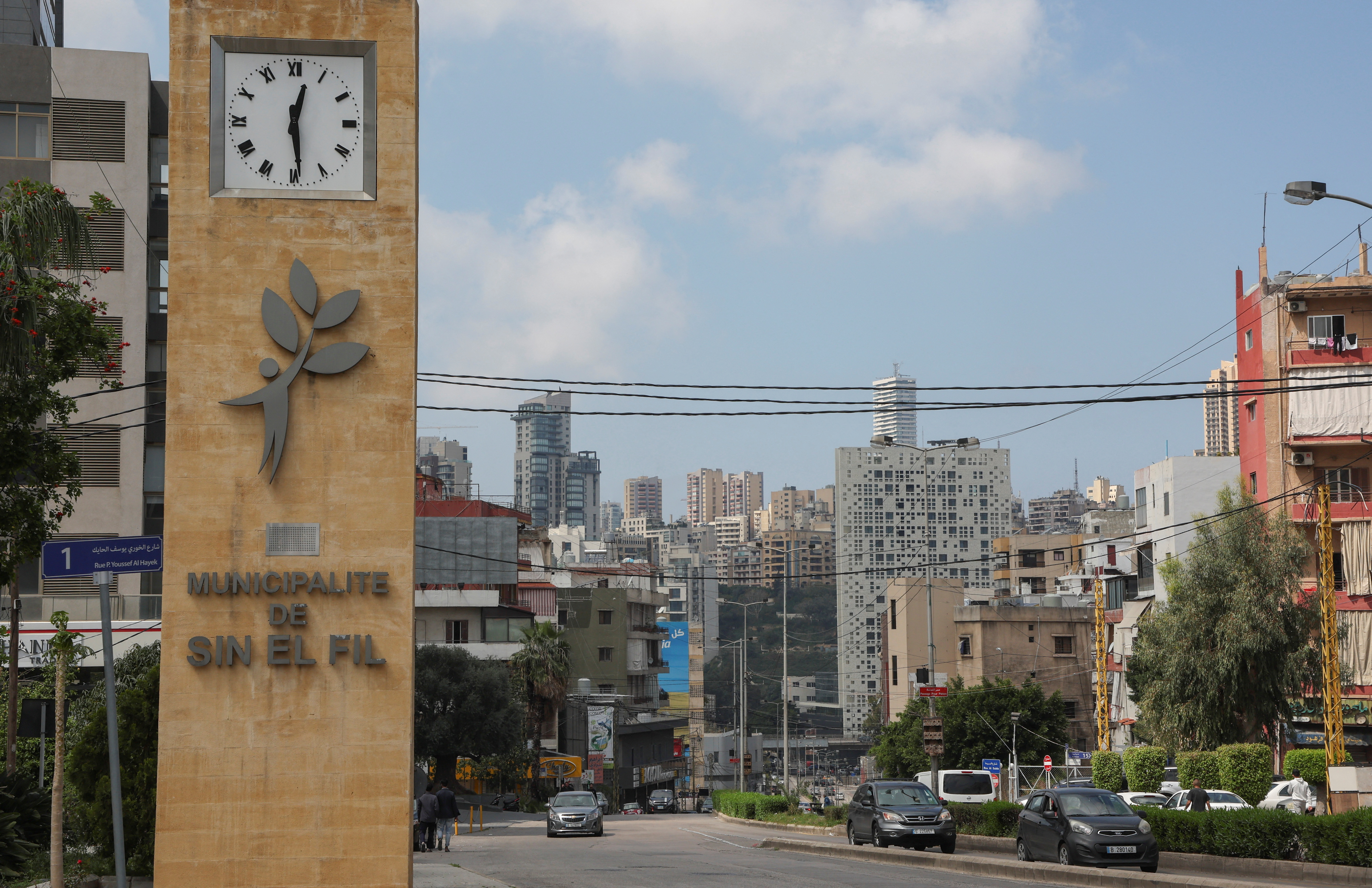 Cars drive near a clock tower using daylight savings time in Sin-el-fil