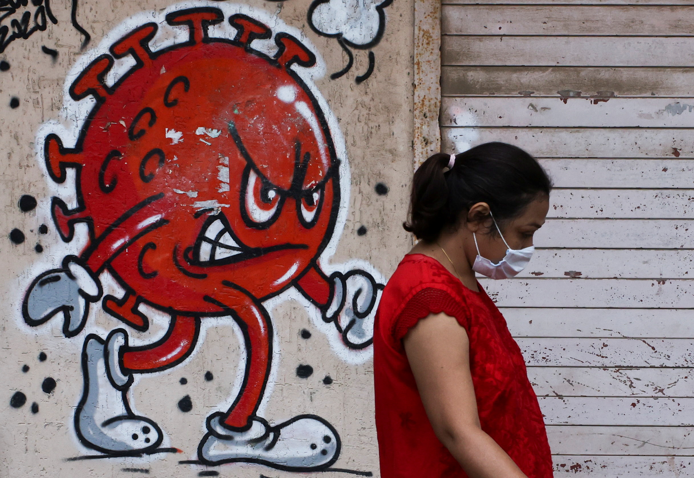 Woman walks past a coronavirus-themed graffiti on a street in Mumbai