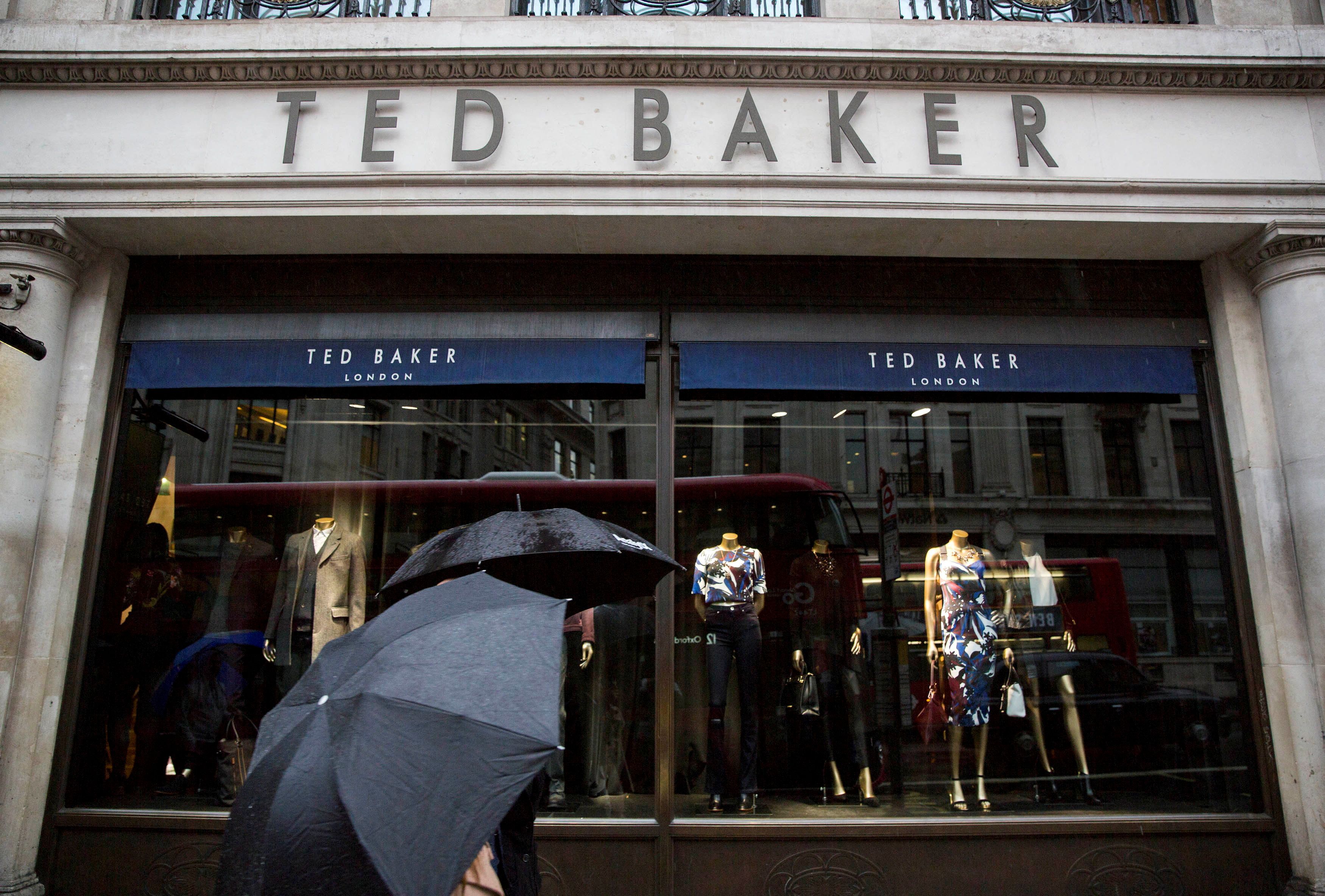 People shelter under umbrellas as they pass a Ted Baker a store in London, Britain