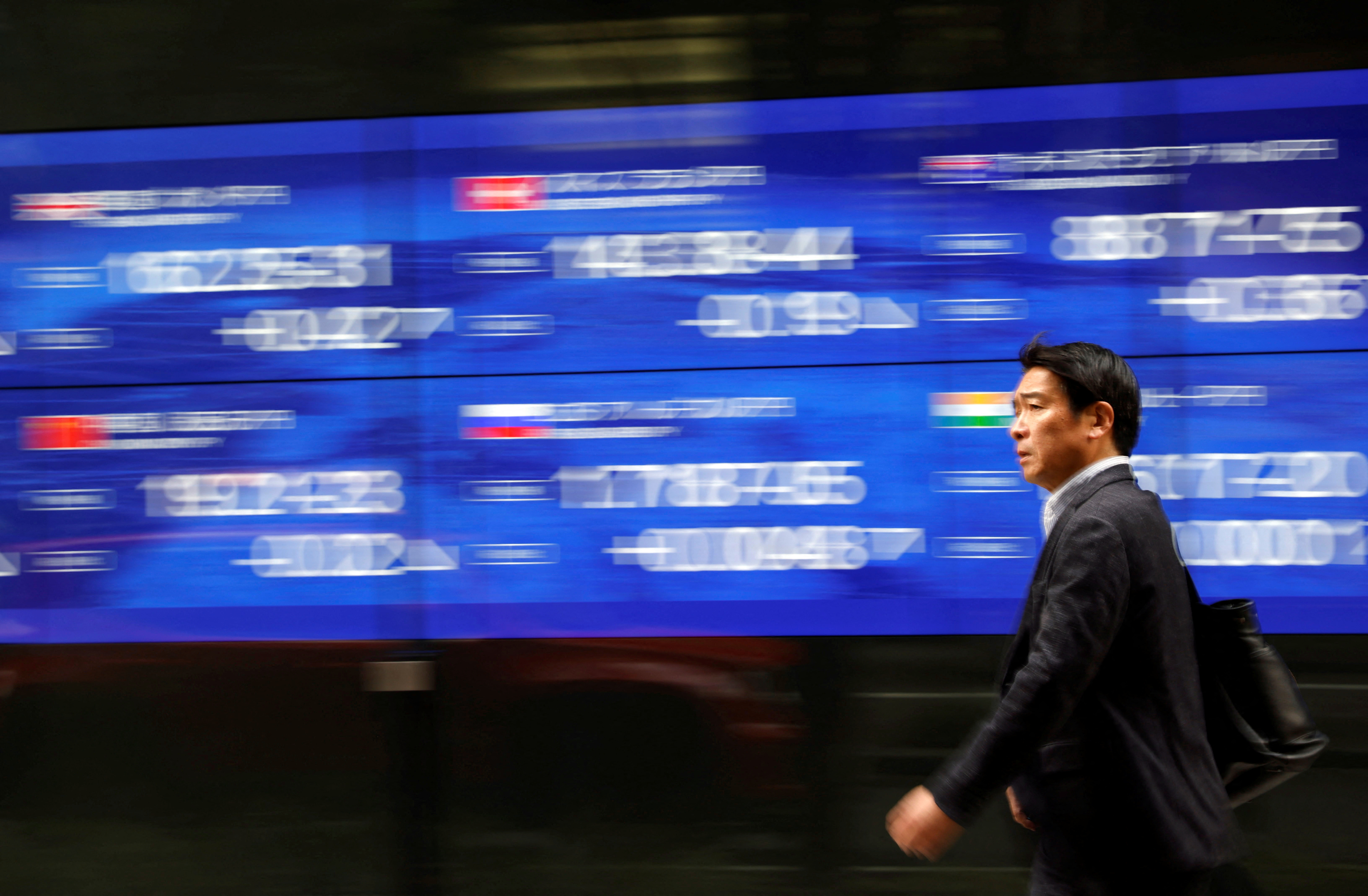 Um transeunte passa por um monitor elétrico exibindo o índice de preços de ações de vários países fora de um banco em Tóquio