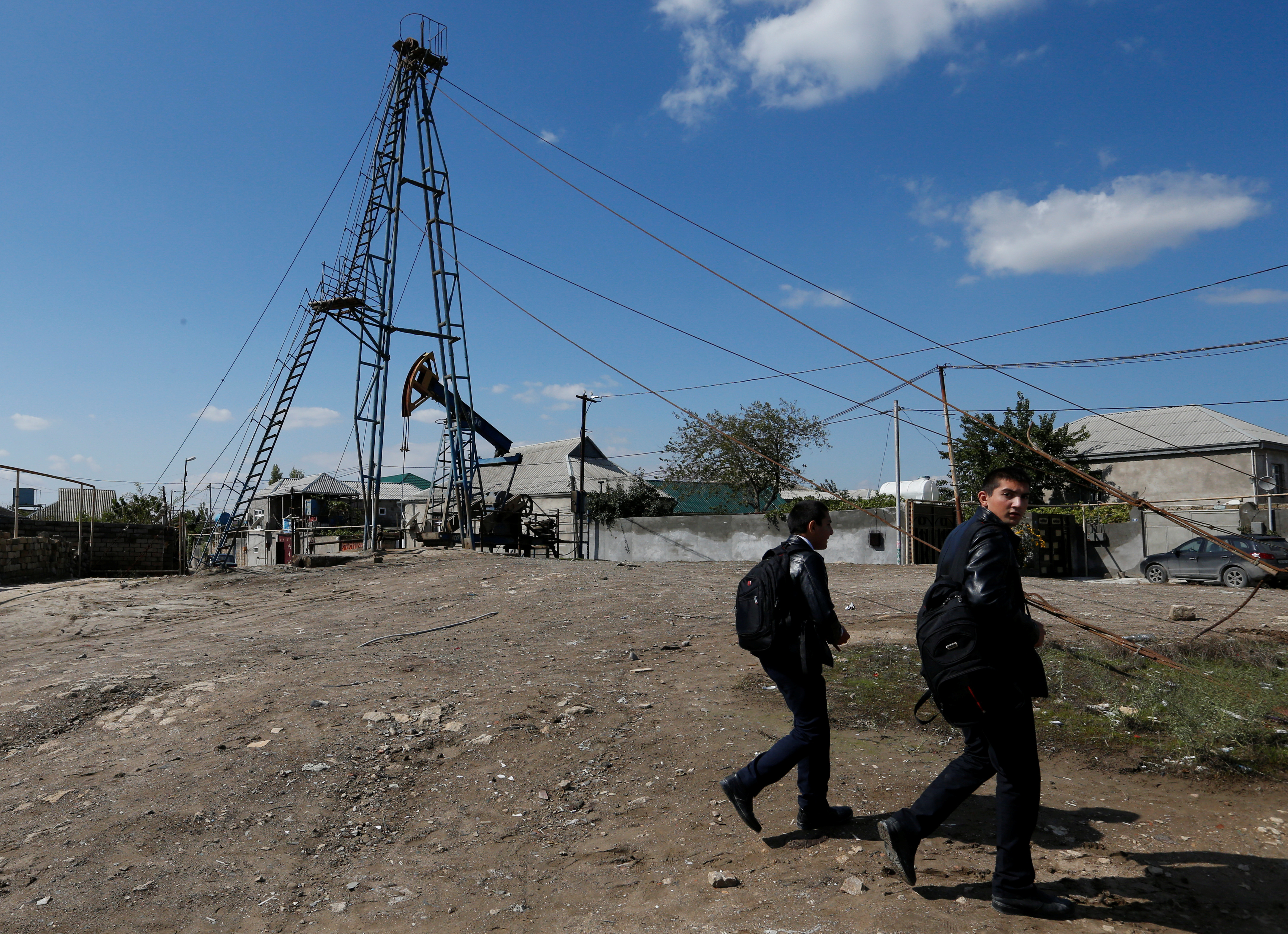 People walk past a nodding donkey pumping oil in the settlement of Balaxani