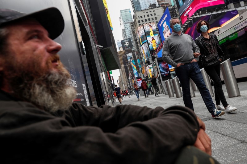 People wearing protective face mask look at Eric Gourley as he sits on the sidewalk outside a closed store at Times Square in New York City