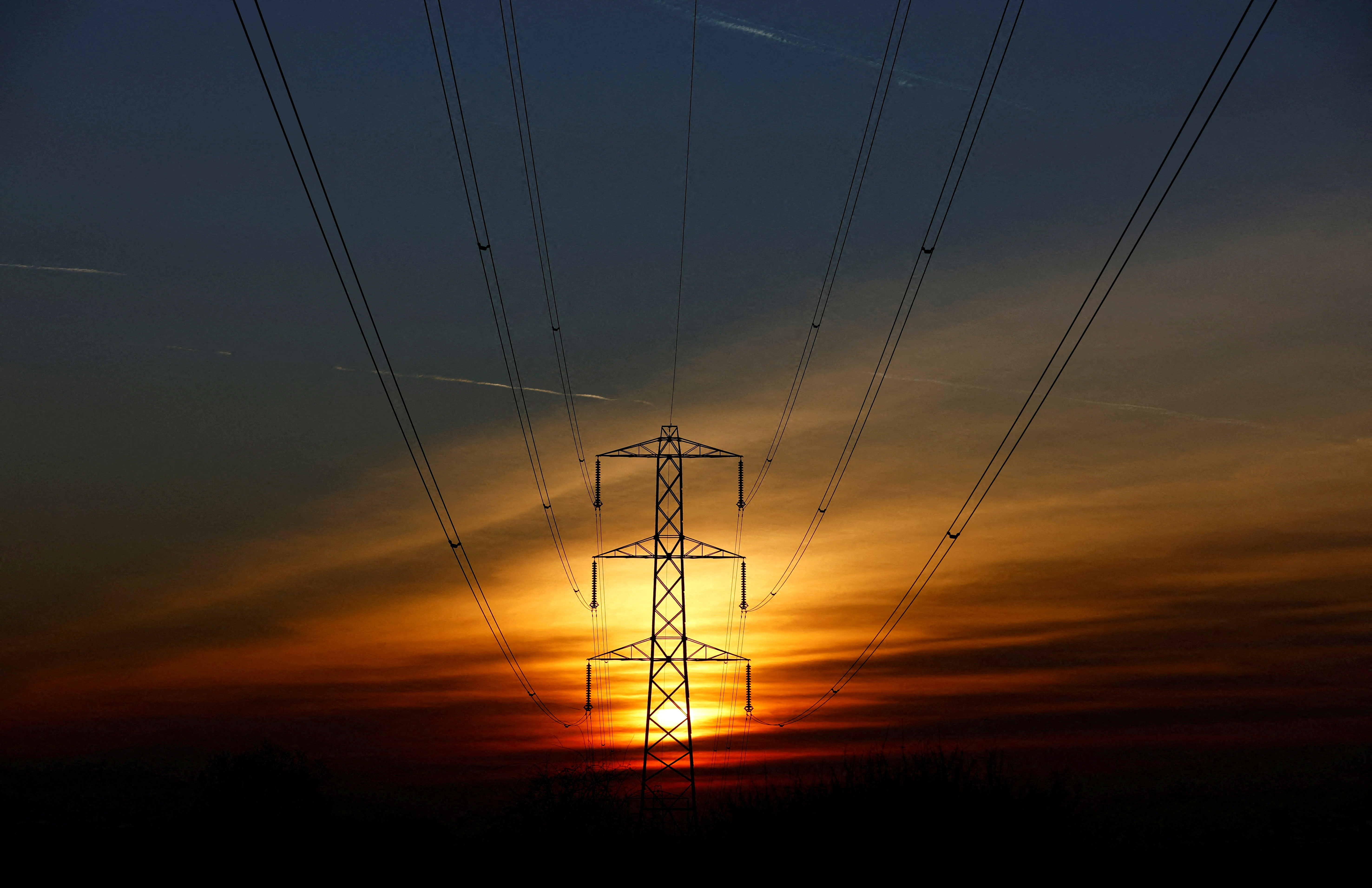 The sun sets behind an electricity pylon in Borehamwood