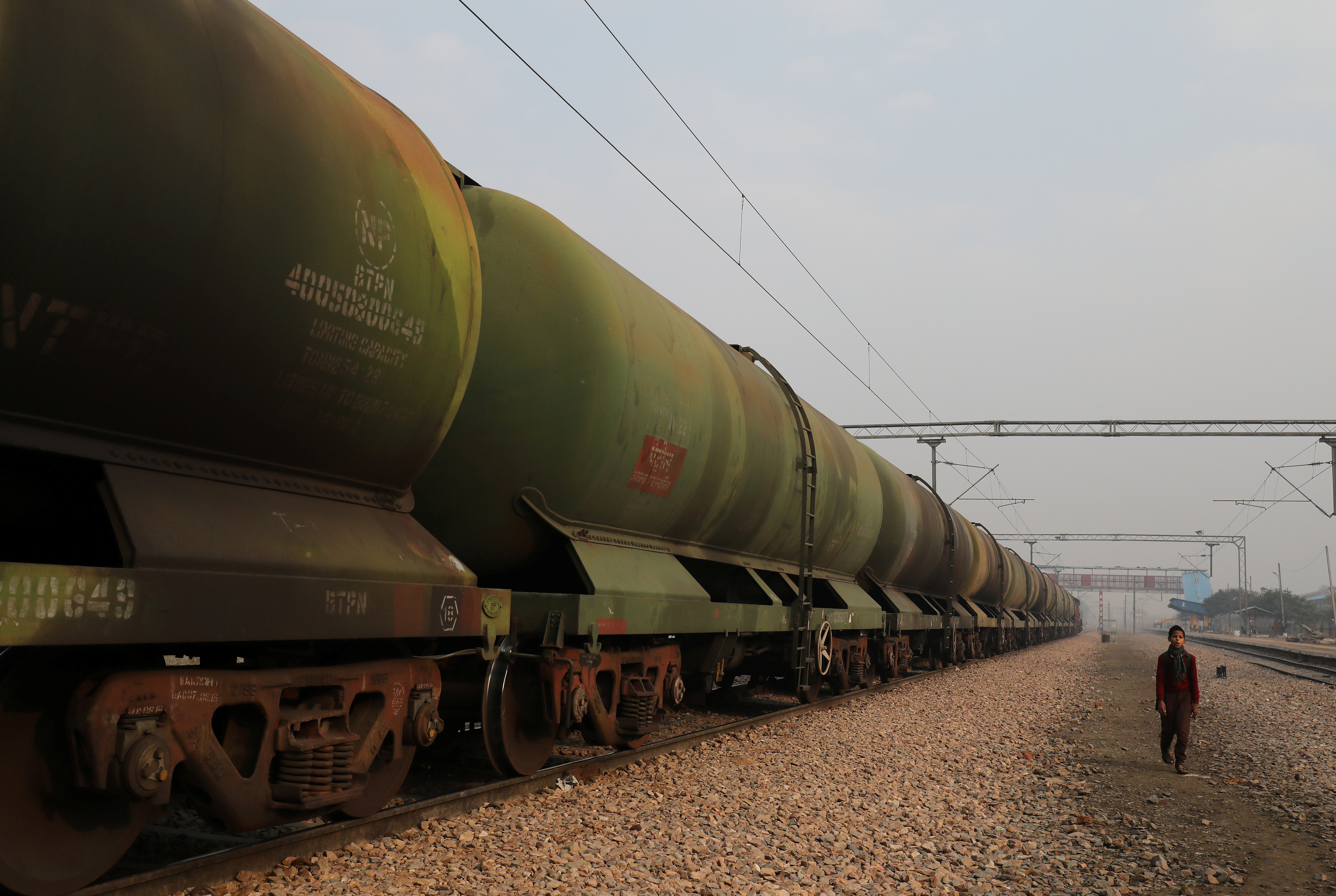 A boy walks past an oil tanker train stationed at a railway station in Ghaziabad