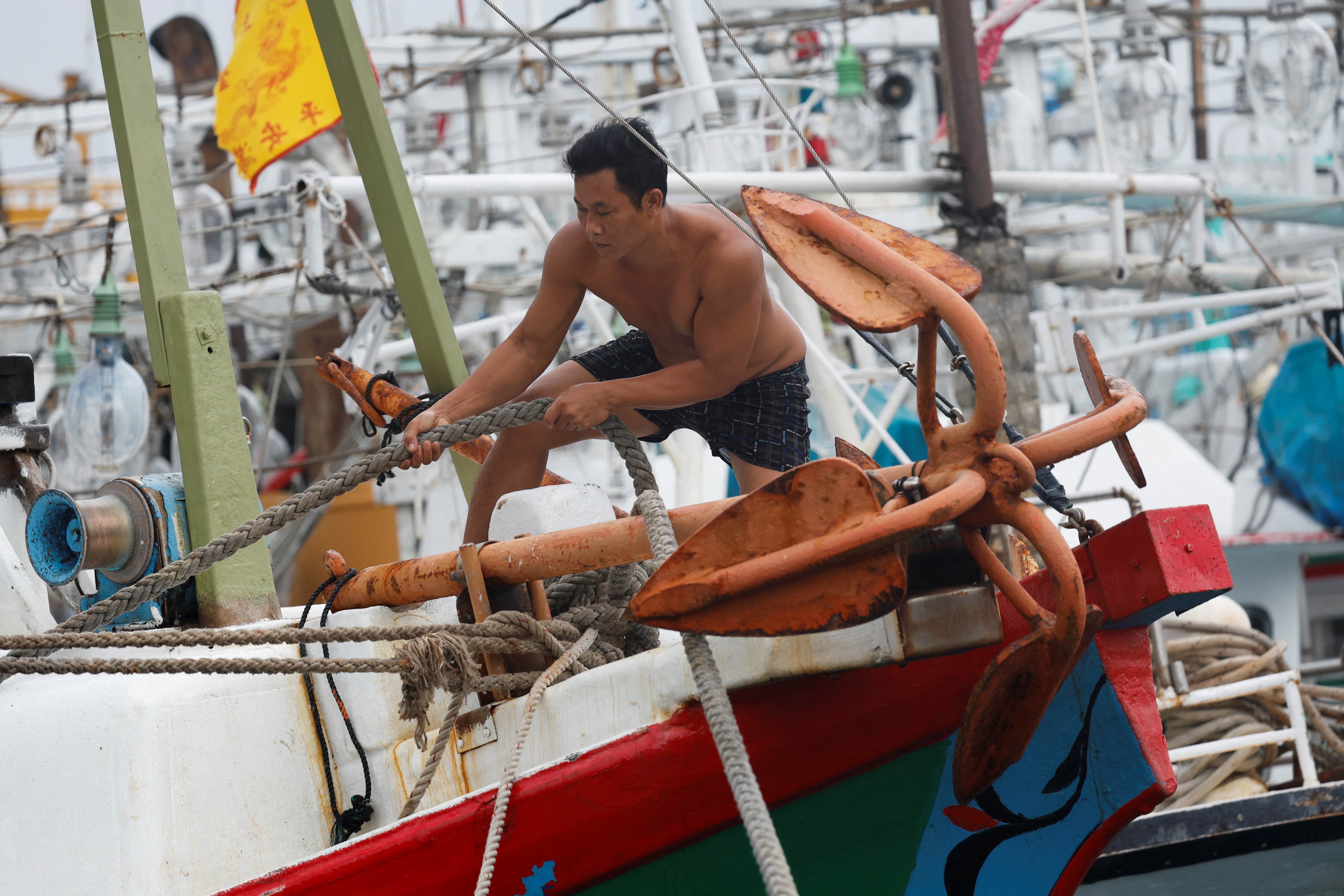 A fisherman tightens a rope on a boat while moored at a fishing harbor as Typhoon Gaemi approaches in Keelung