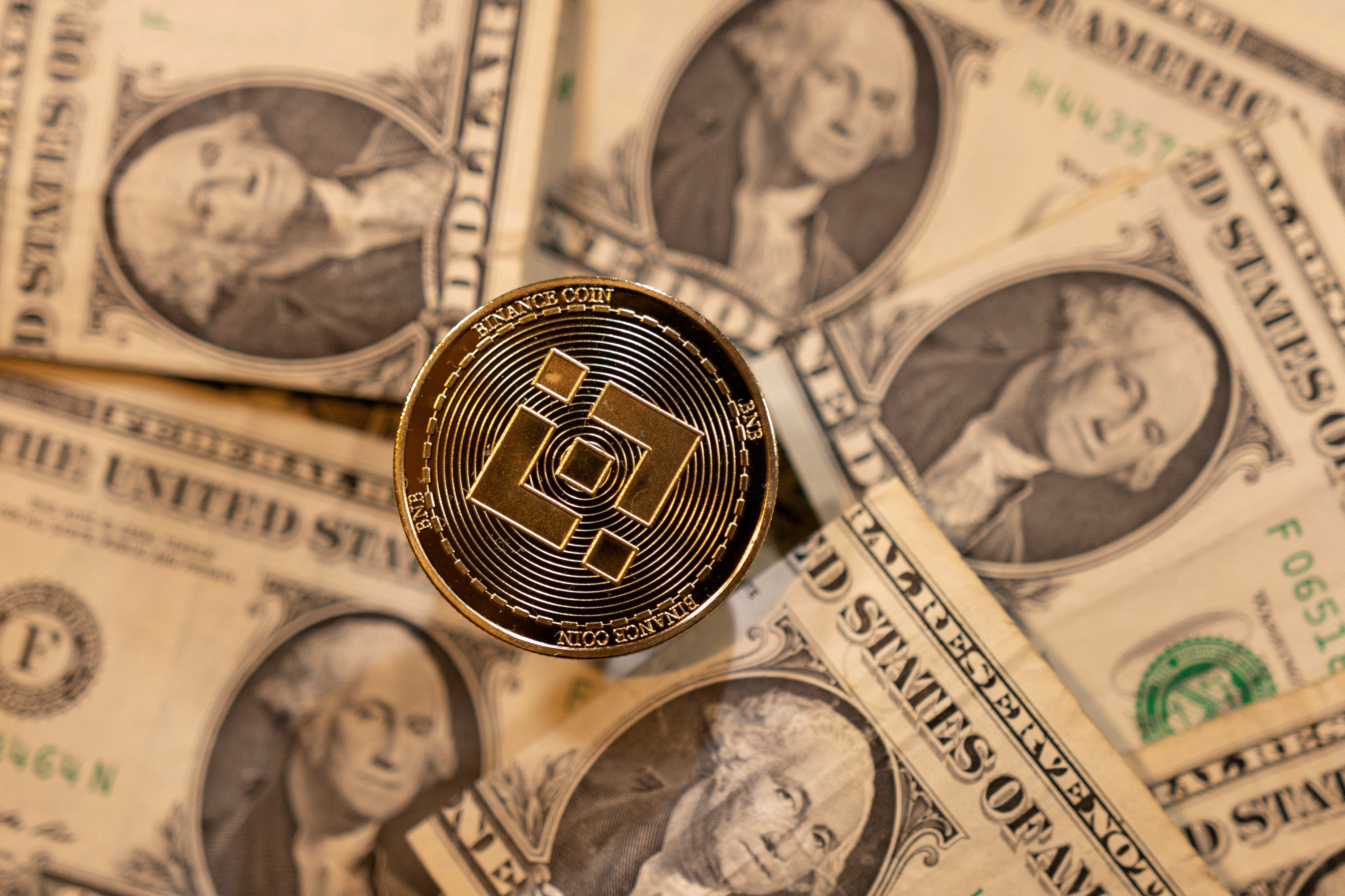 Illustration shows coin representation of cryptocurrency exchange Binance and U.S. dollar banknotes
