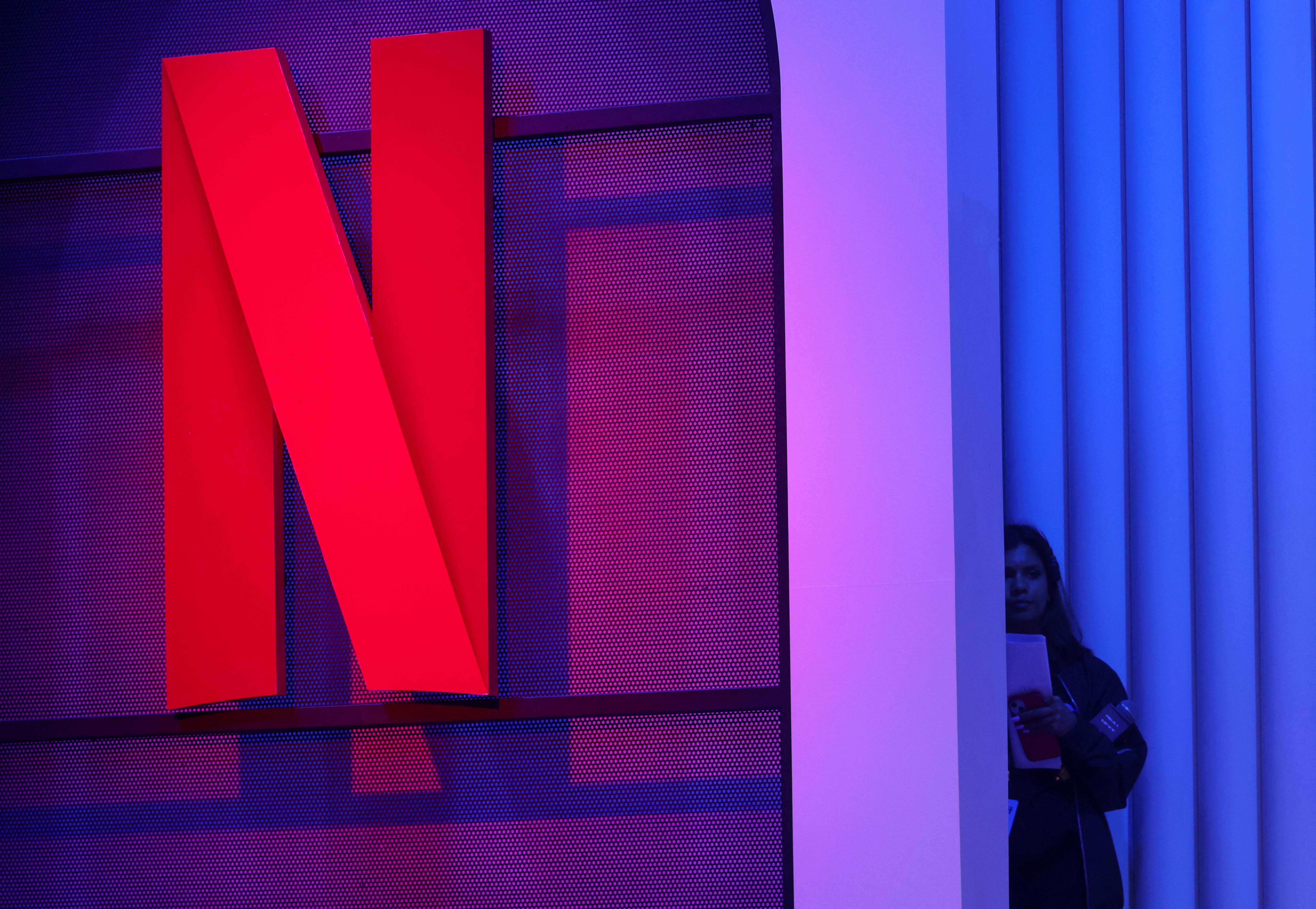 A woman stands next to a logo of Netflix during an event in Mumbai