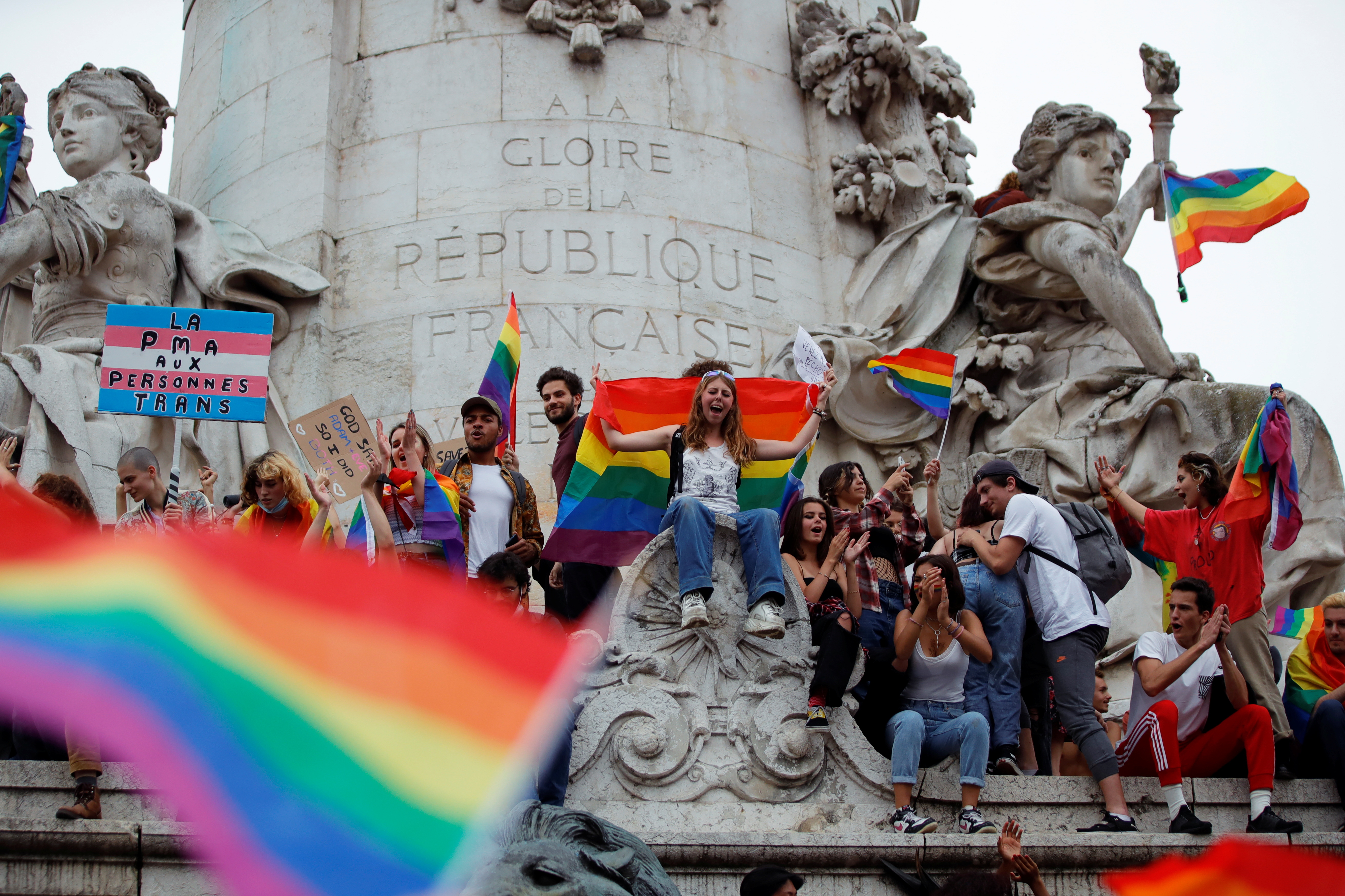 Teilnehmer mit Regenbogenfahnen und Plakaten sitzen während des traditionellen LGBTQ-Pride-Marsches inmitten des Ausbruchs der Coronavirus-Krankheit (COVID-19) auf dem Platz der Republik in Paris, Frankreich, 26. Juni 2021 auf einem Denkmal. REUTERS/Sarah Meyssonnier