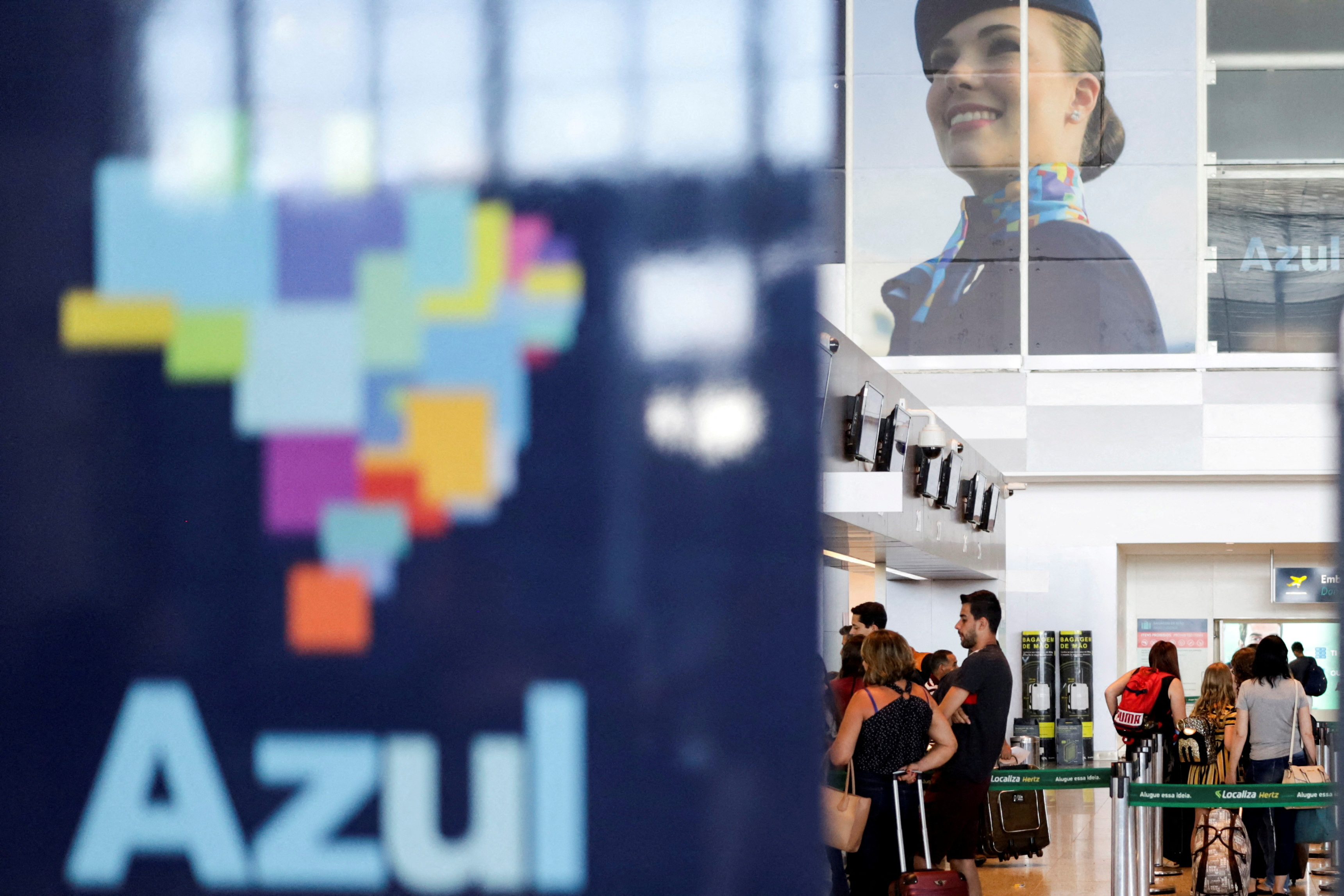 Passengers stand near a Brazilian airline Azul signage, after the airline stated that it will cut all of its international flights out from its main hub due to the coronavirus outbreak, at Viracopos International Airport, in Campinas