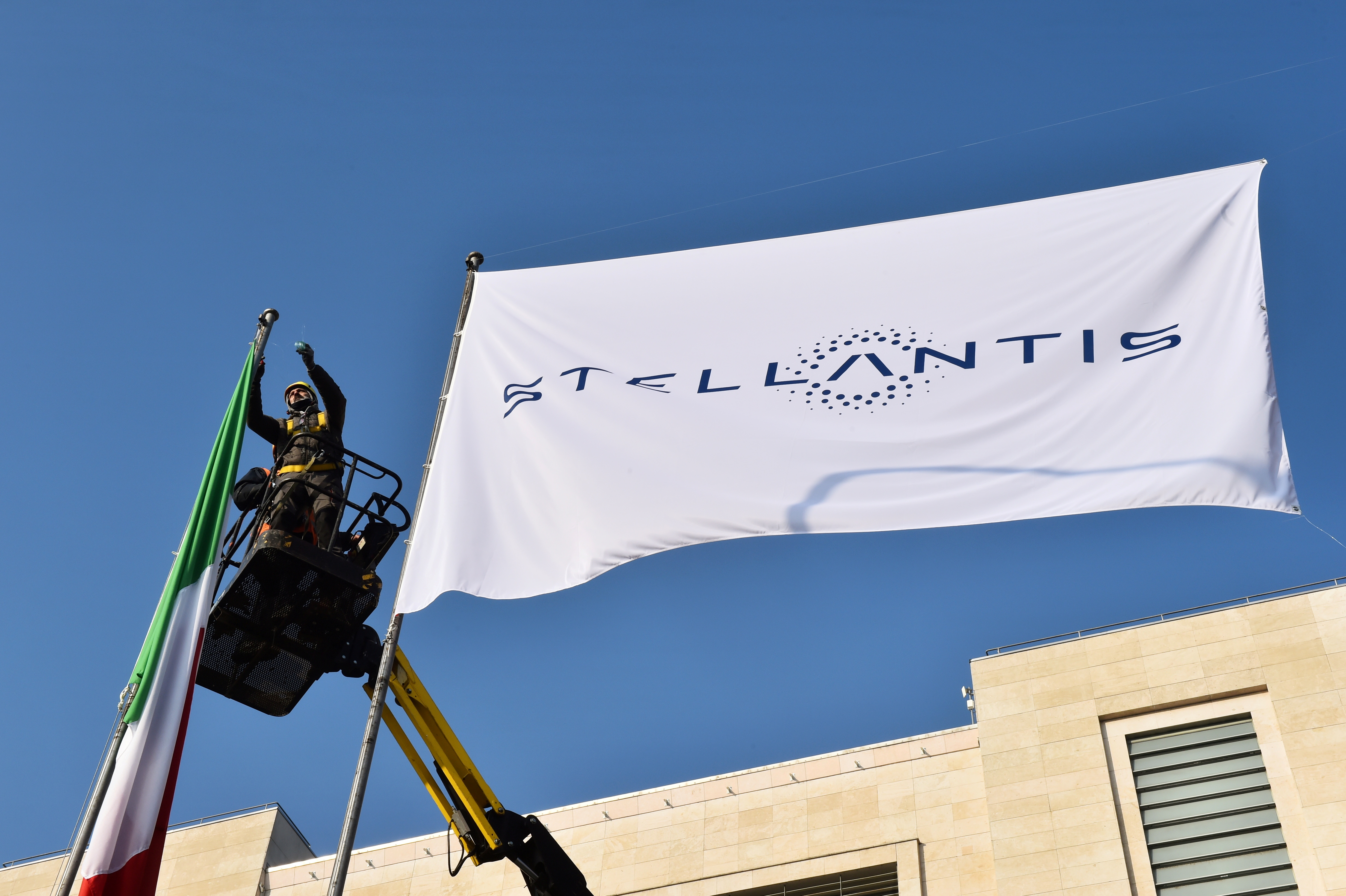 Workers install a flag with the logo of Stellantis, the world's fourth-largest automaker which starts trading in Milan and Paris after Fiat Chrysler and Peugeot maker PSA finalised their merger, at the main entrance of FCA Mirafiori plant in Turin, Italy, January 18, 2021. REUTERS/Massimo Pinca