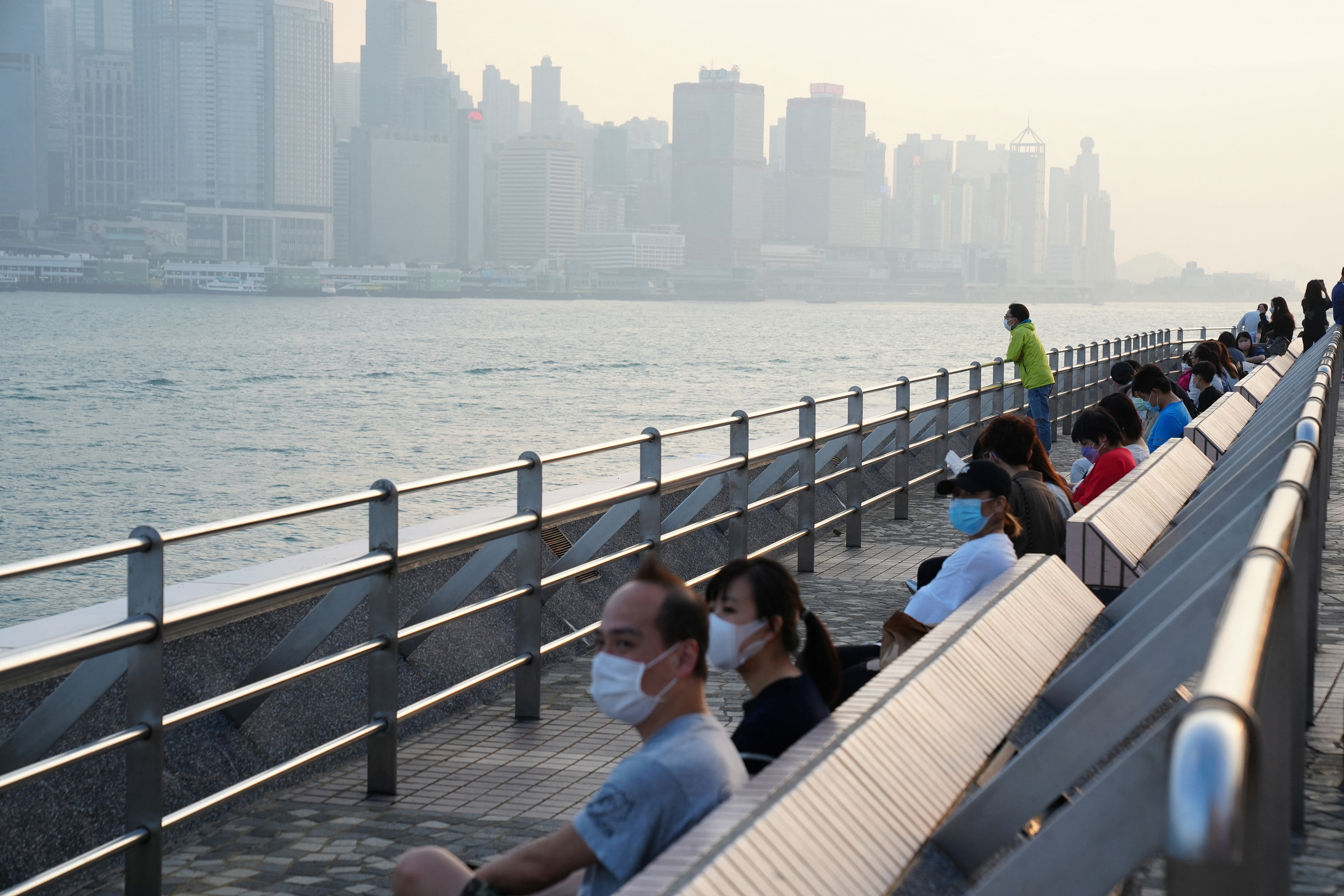 People wearing face masks sit at the seaside nearby Victoria Harbour, after the government eased the coronavirus disease (COVID-19) restrictions on businesses, in Tsim Sha Tsui district in Hong Kong