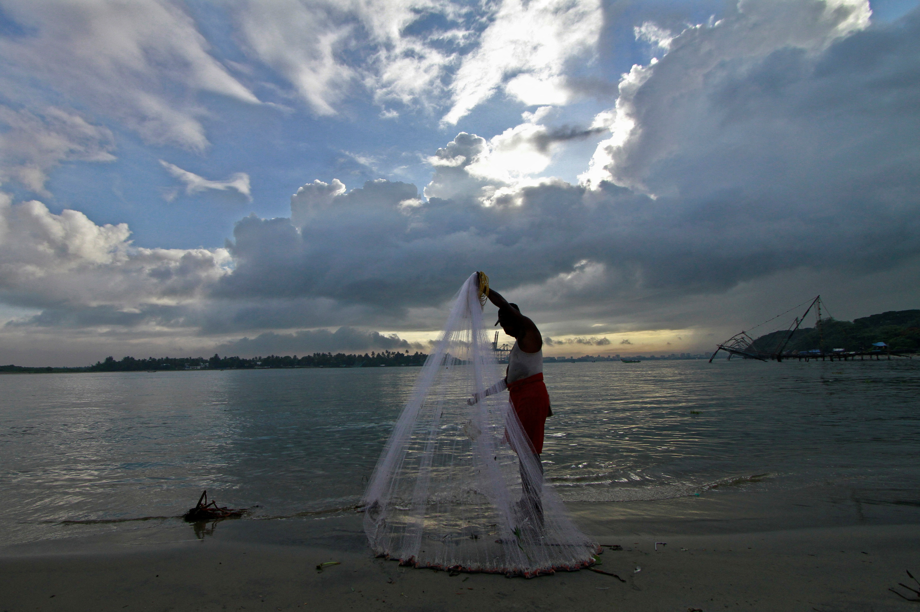 A fisherman arranges his fishing net at a beach against the backdrop of pre-monsoon clouds in Kochi
