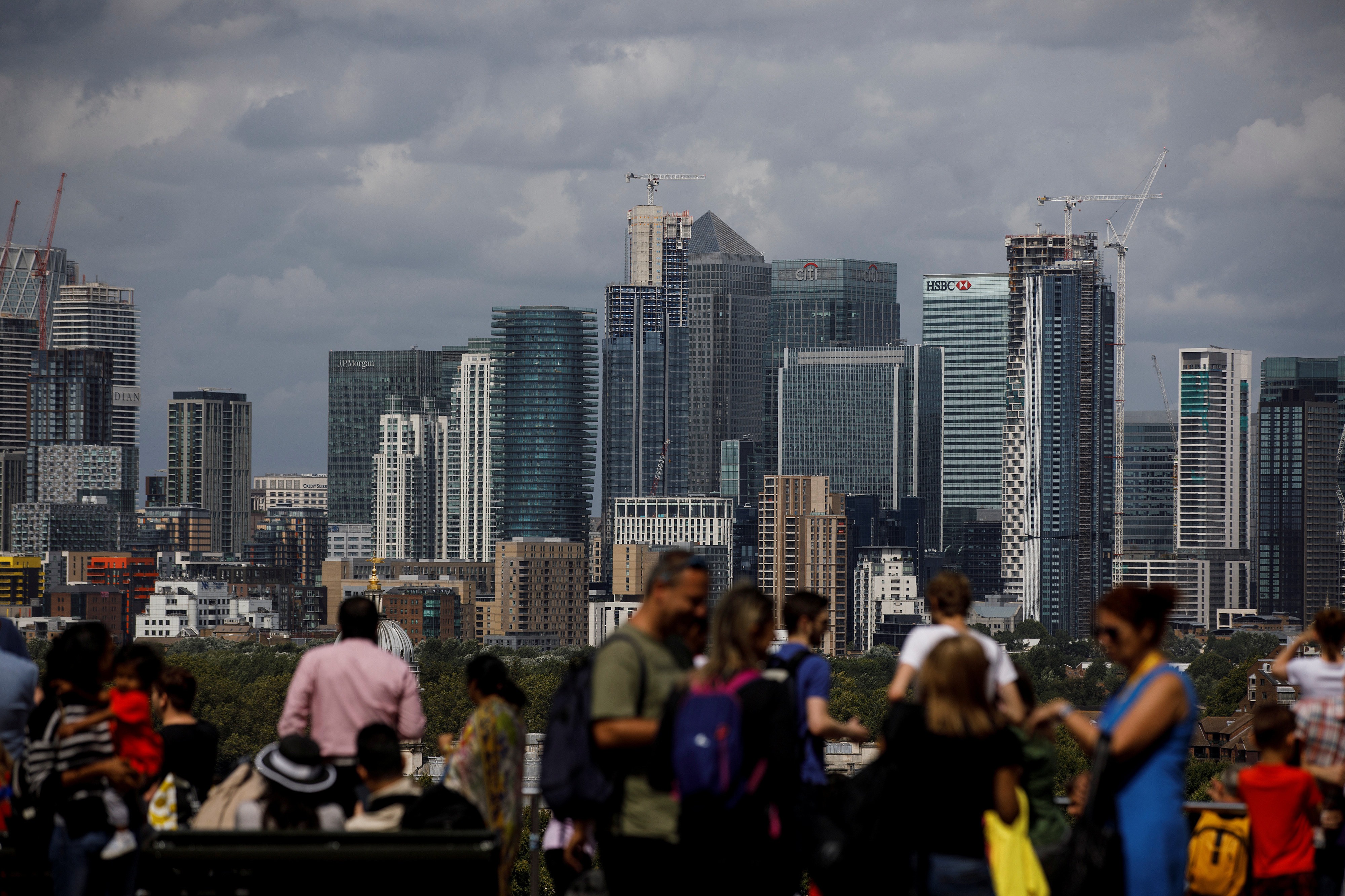 People look out onto the Canary Wharf financial district as they stand at a viewing area in Greenwich Park in London