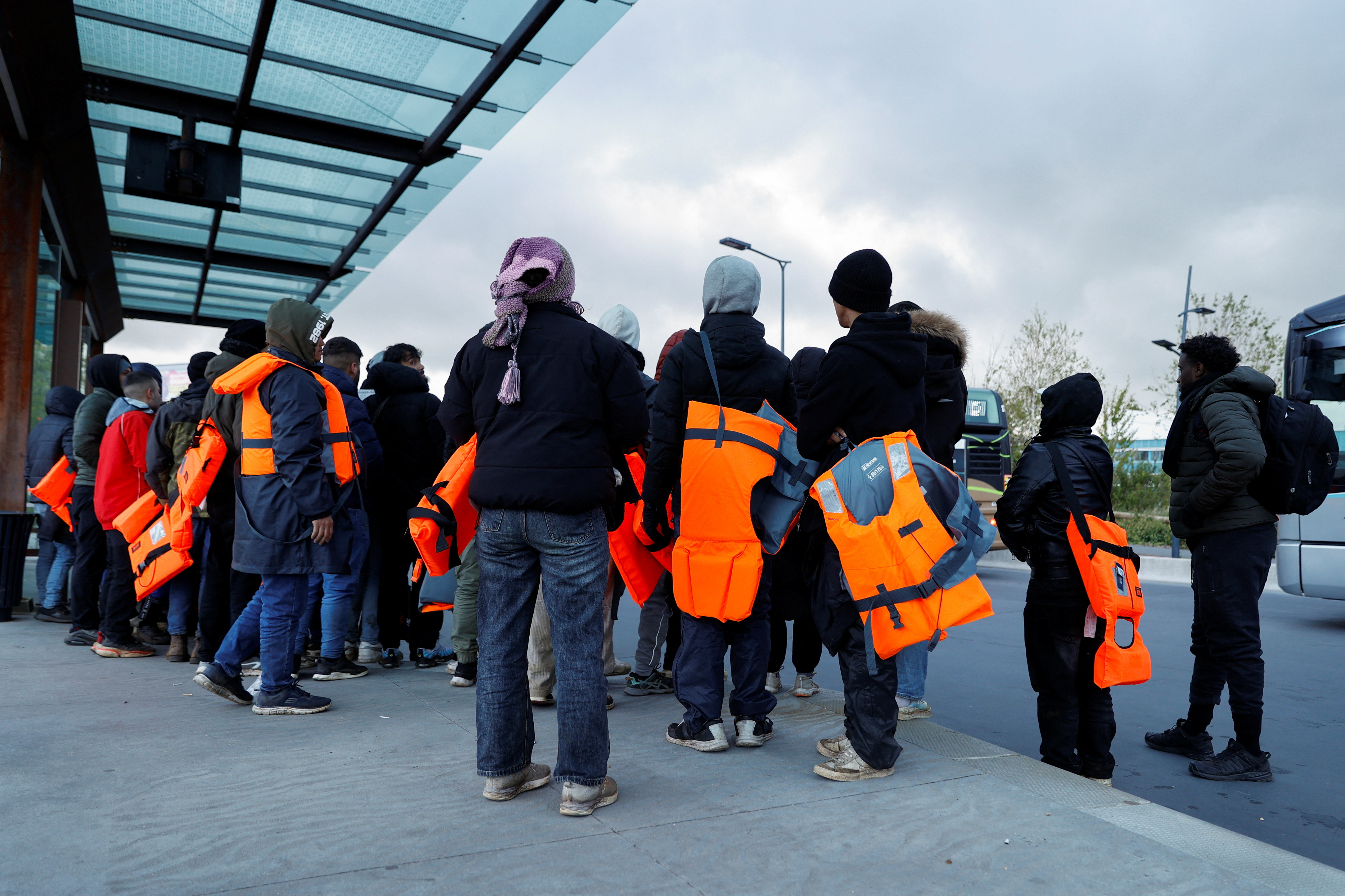 Migrants wait for a bus to return from the beach to their camp, at Calais train station