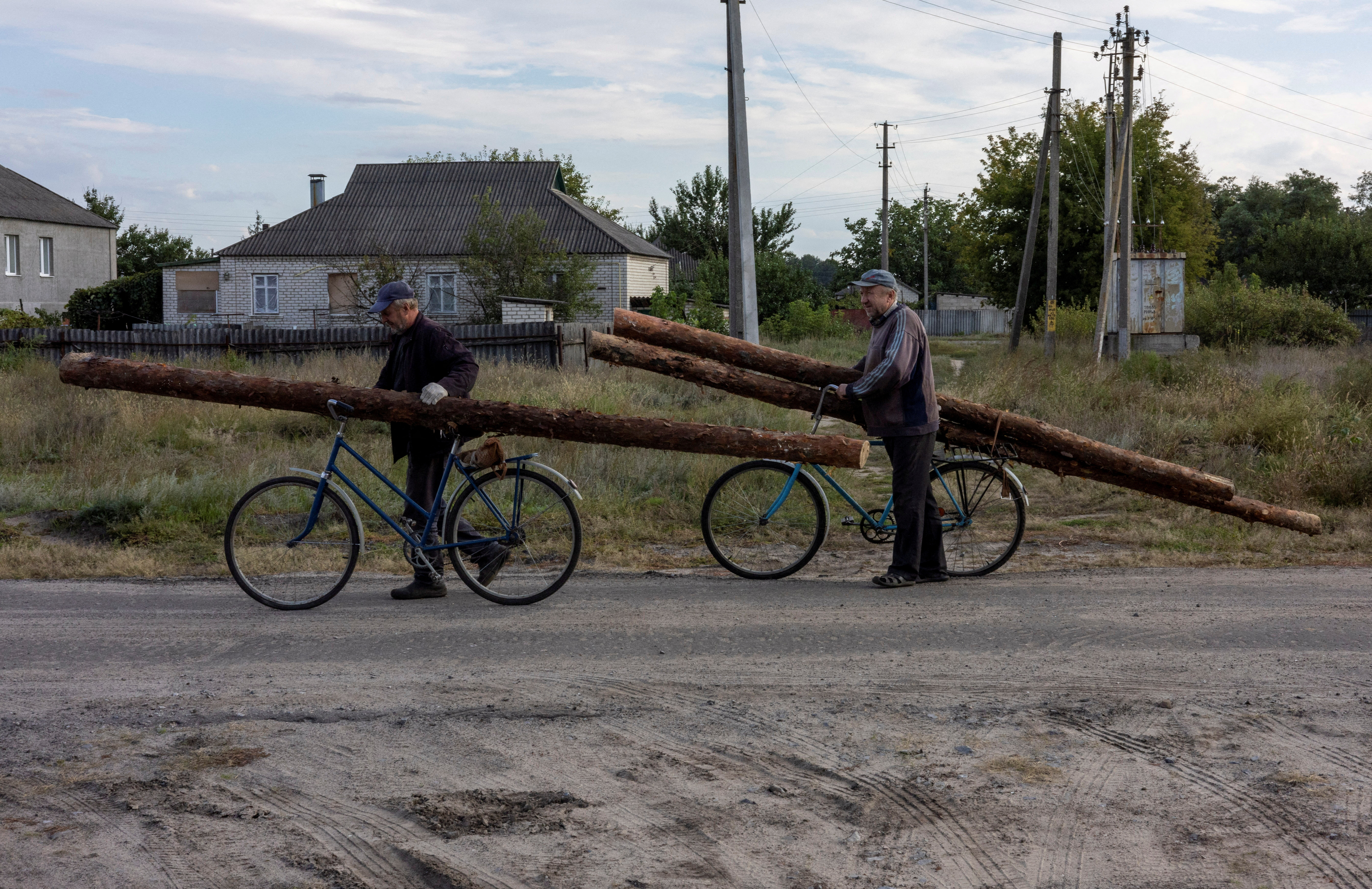 Men carry wood collected from abandoned Russian military bunkers, on their bicycles to use for heating during the winter, in Izium