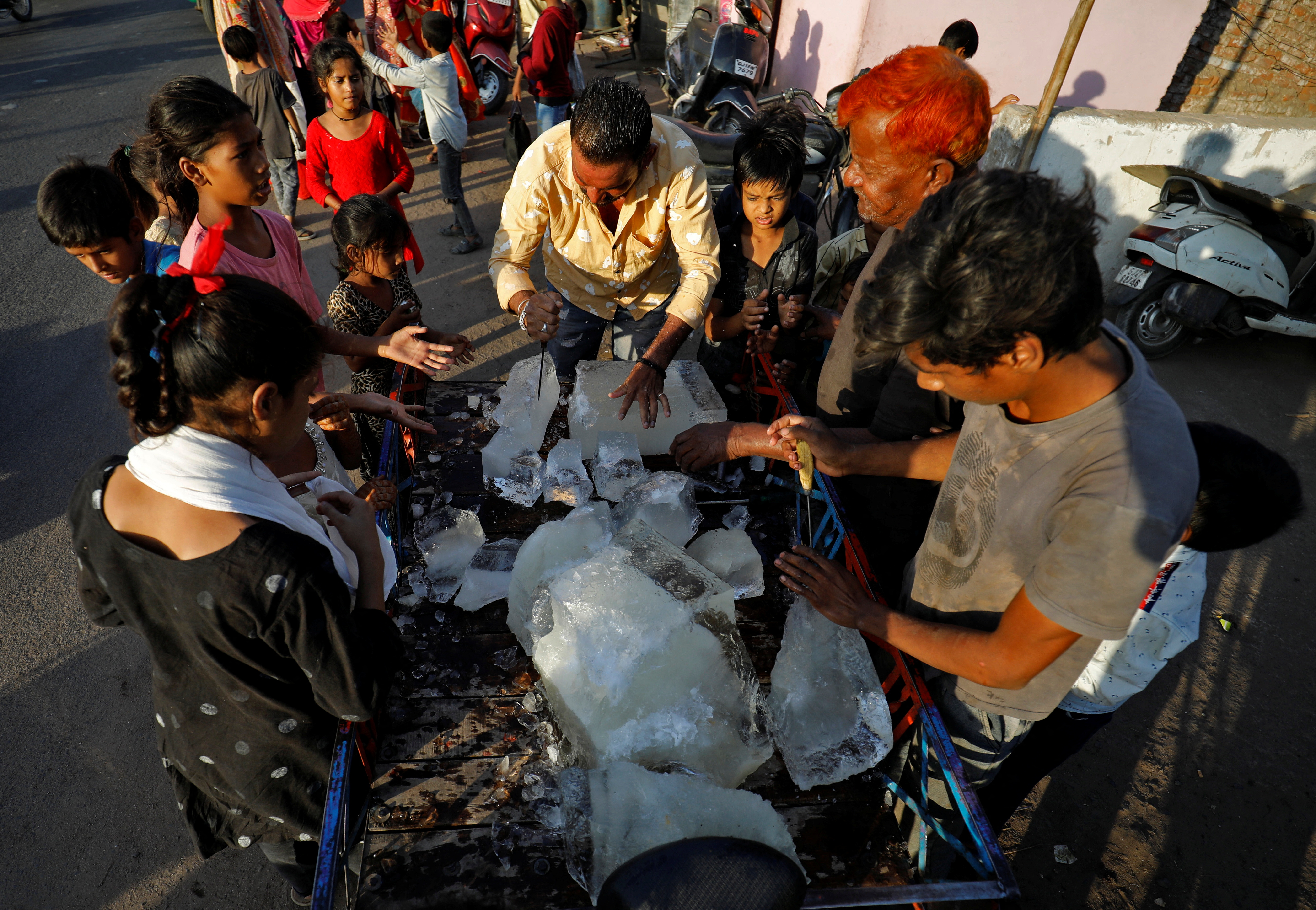 A man breaks a block of ice to distribute it among the residents of a slum during hot weather in Ahmedabad