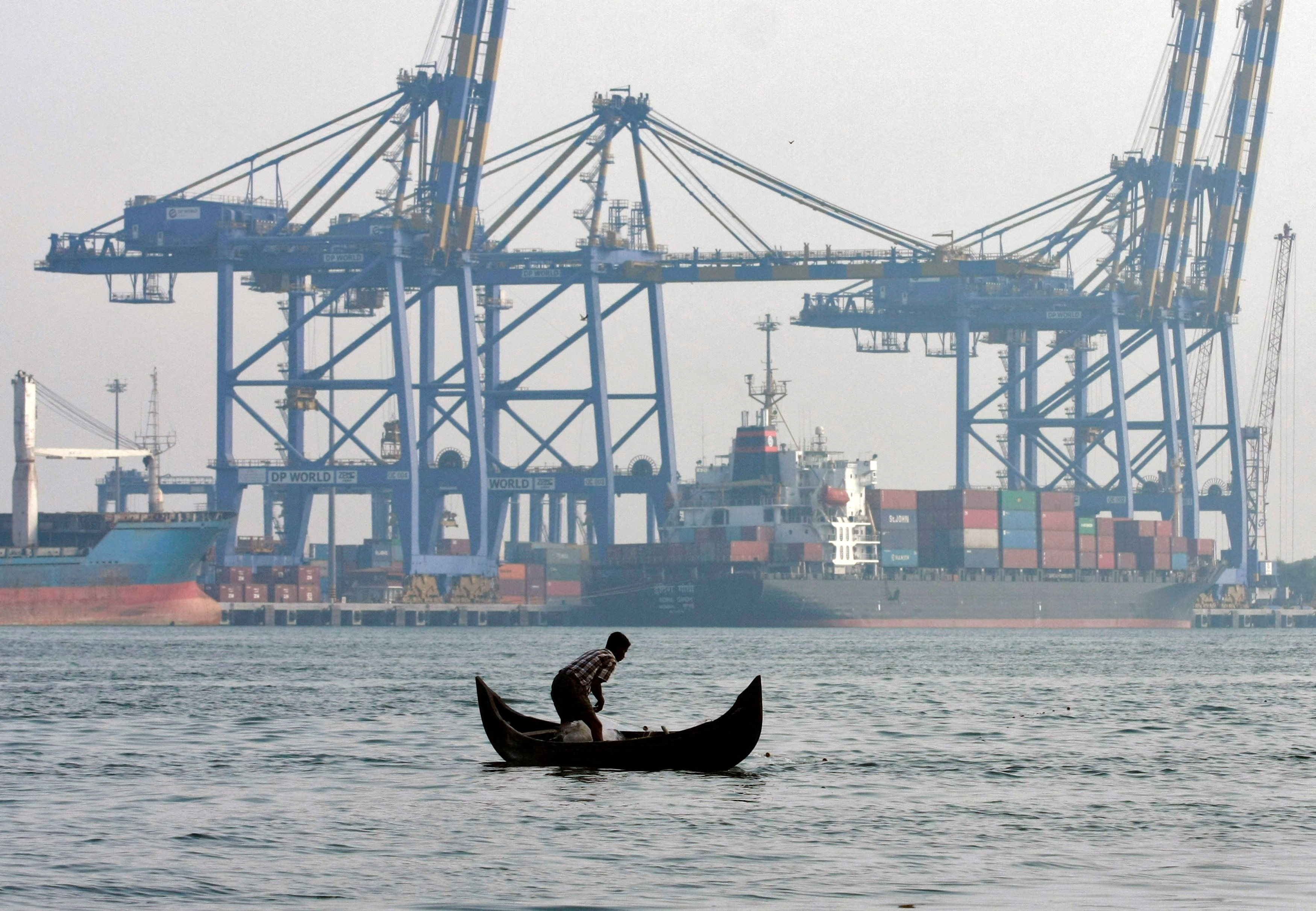 Fisherman prepares to cast his fishing net in waters of Vembanad lake as a container ship is seen docked in the background at a port in Vallarpadam in Kochi