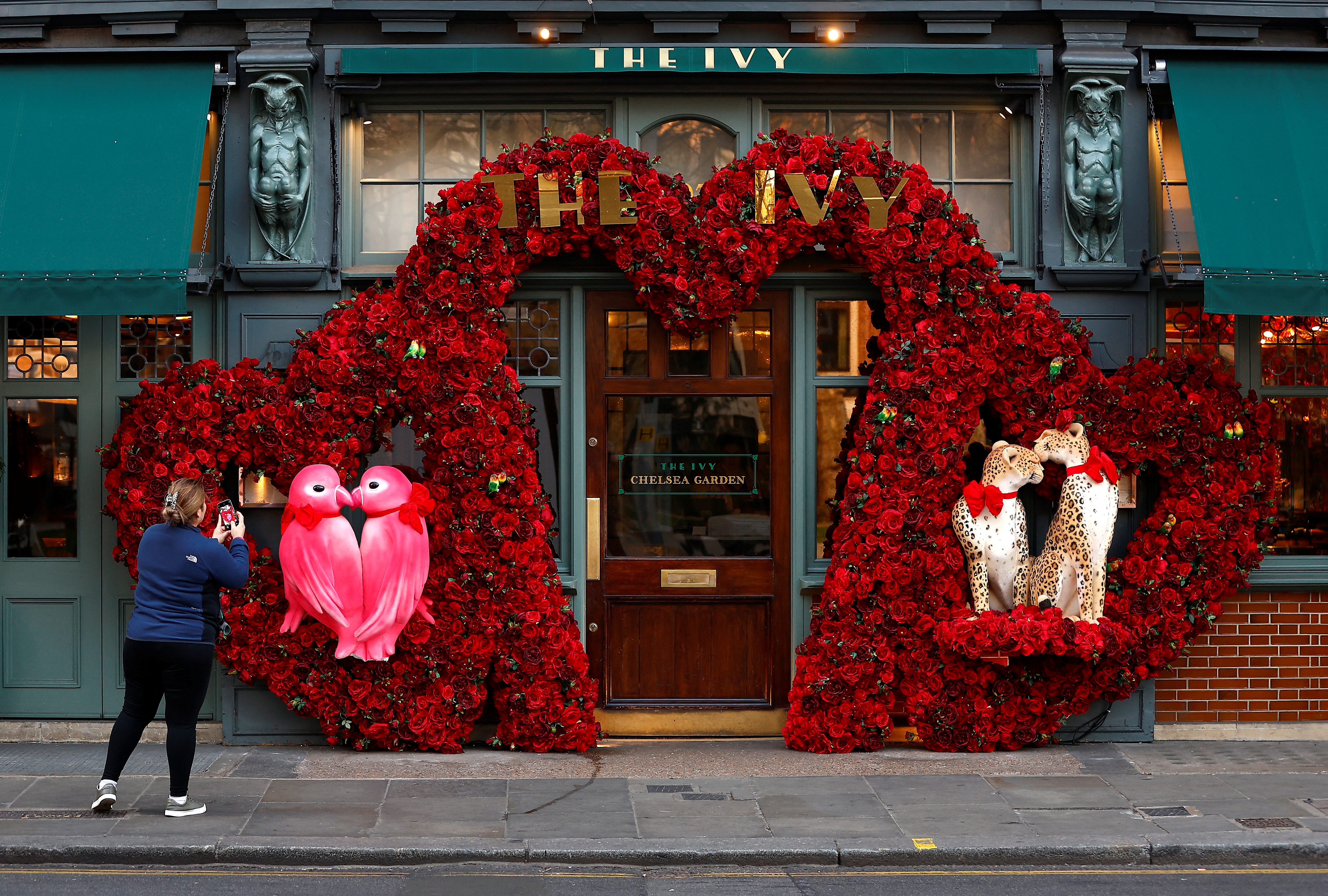 A woman photographs a Valentines Day floral display attached to the facade of a restaurant in London