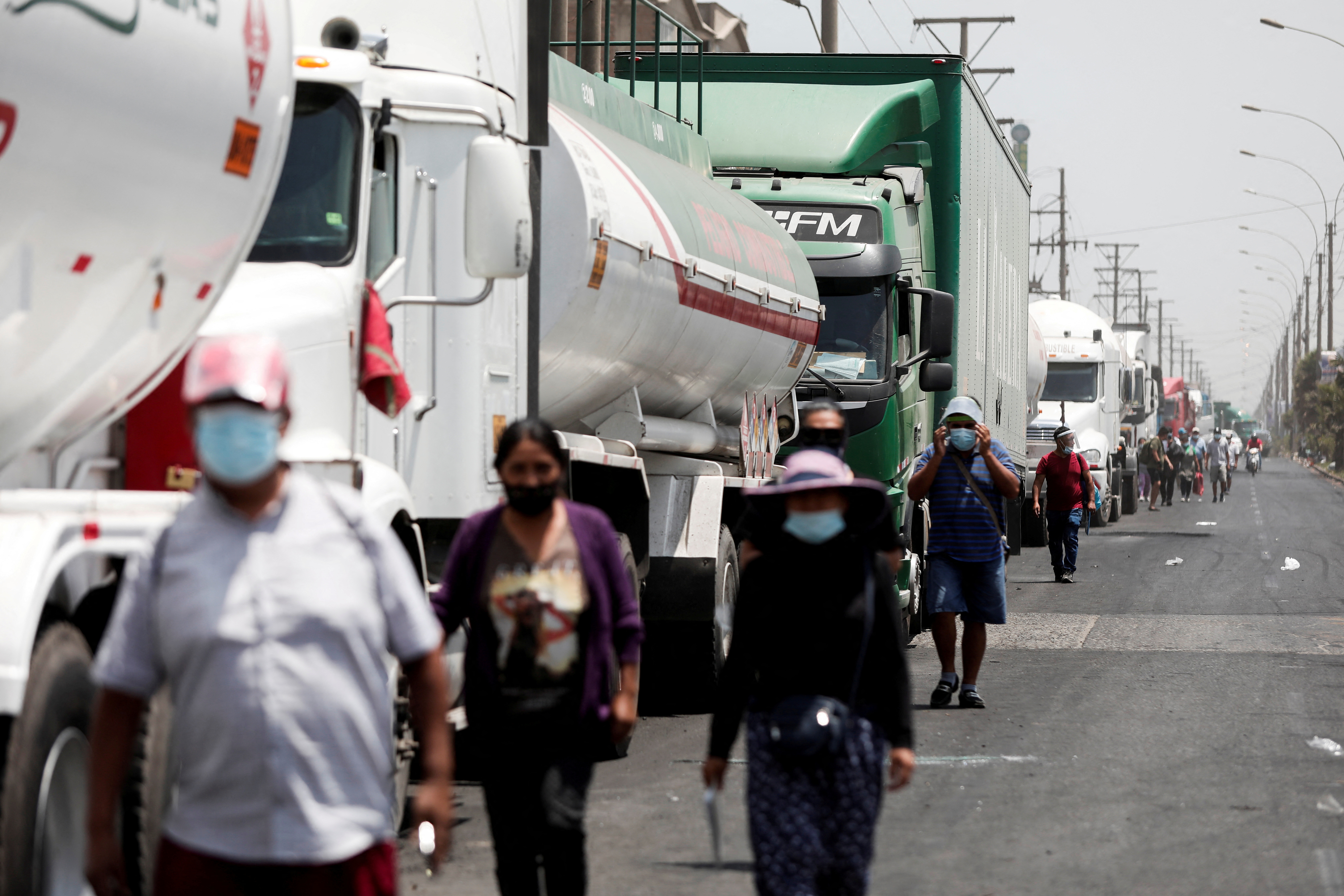 People walk next to parked trucks during a national transportation strike against fuel prices, in Lima