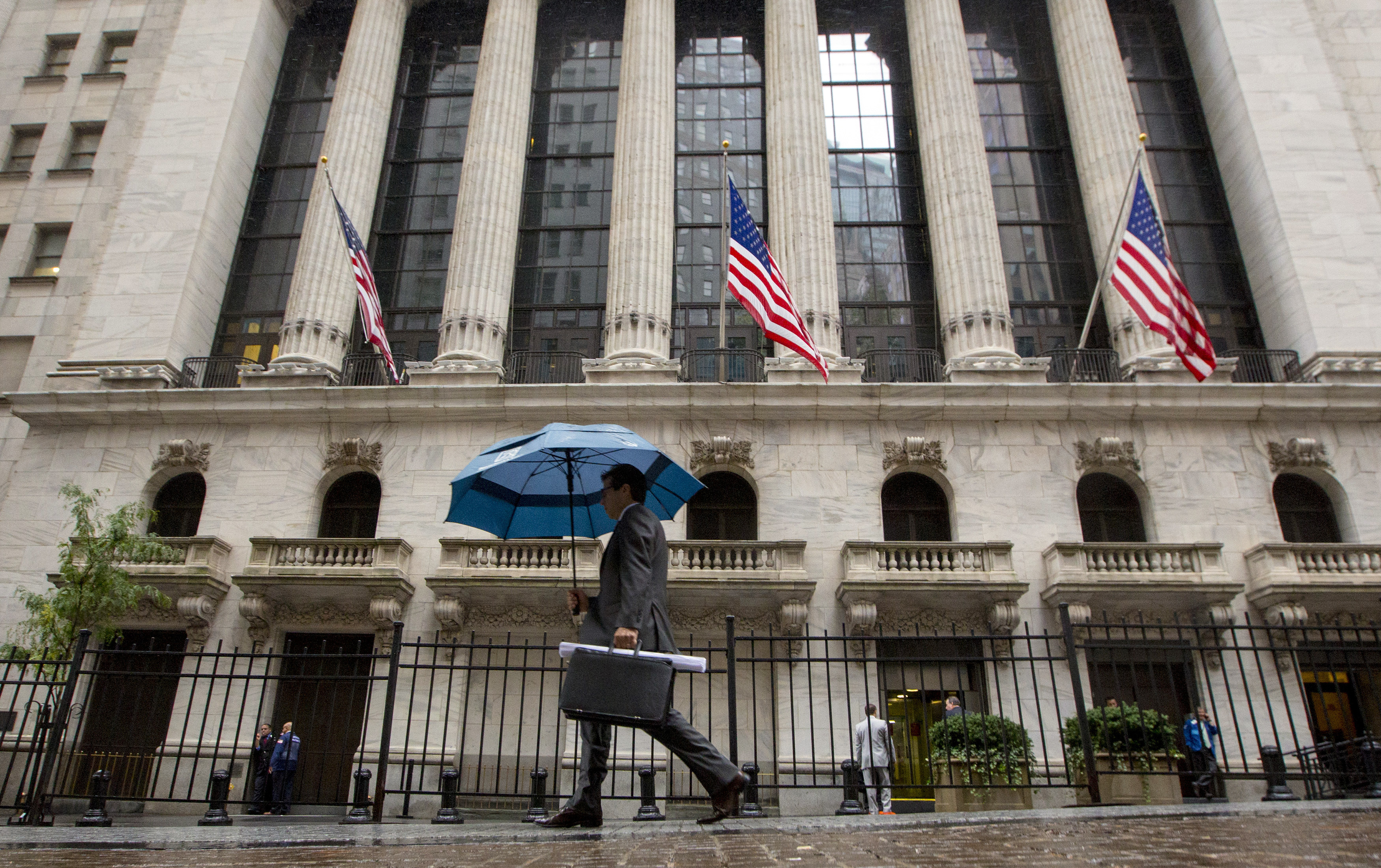 Man carries an umbrella in the rain as he passes the New York Stock Exchange