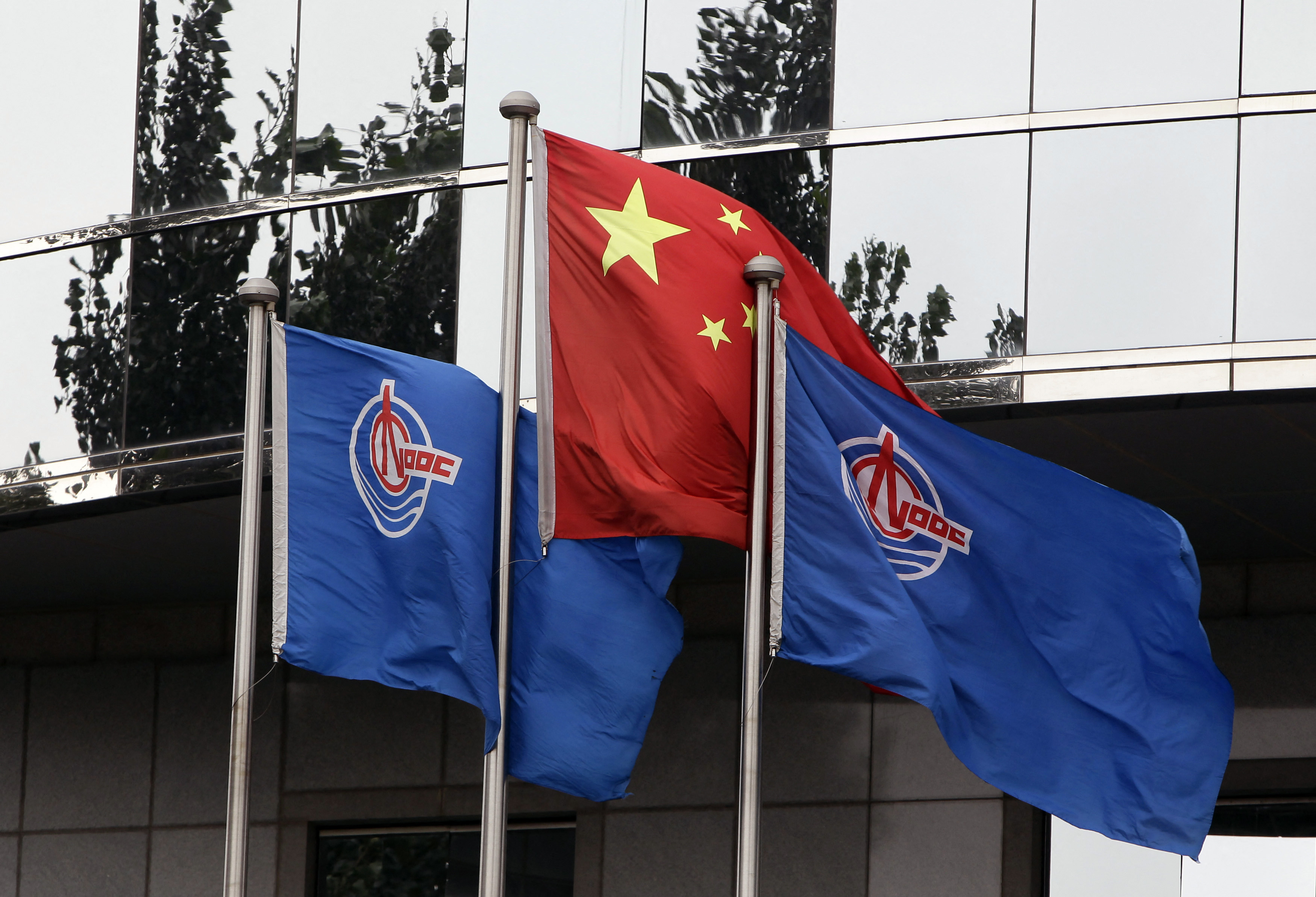Flags of China National Offshore Oil Corp (CNOOC) fly beside the China flag in front of its headquarters building in Beijing