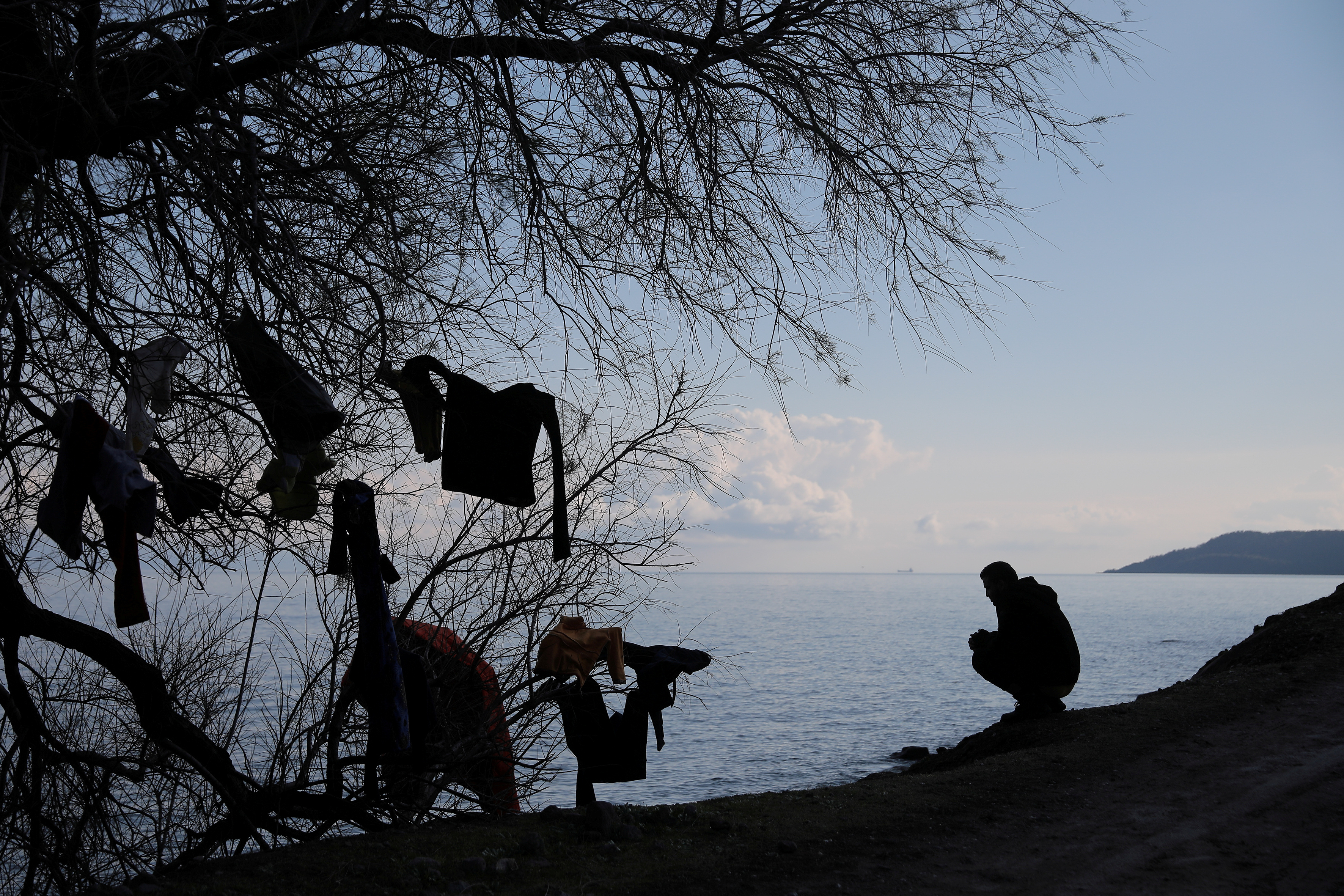 A migrant, who arrived the previous day on a dinghy after crossing part of the Aegean Sea from Turkey, sits next to a tree where clothes are left to dry, near the village of Skala Sikamias, on the island of Lesbos