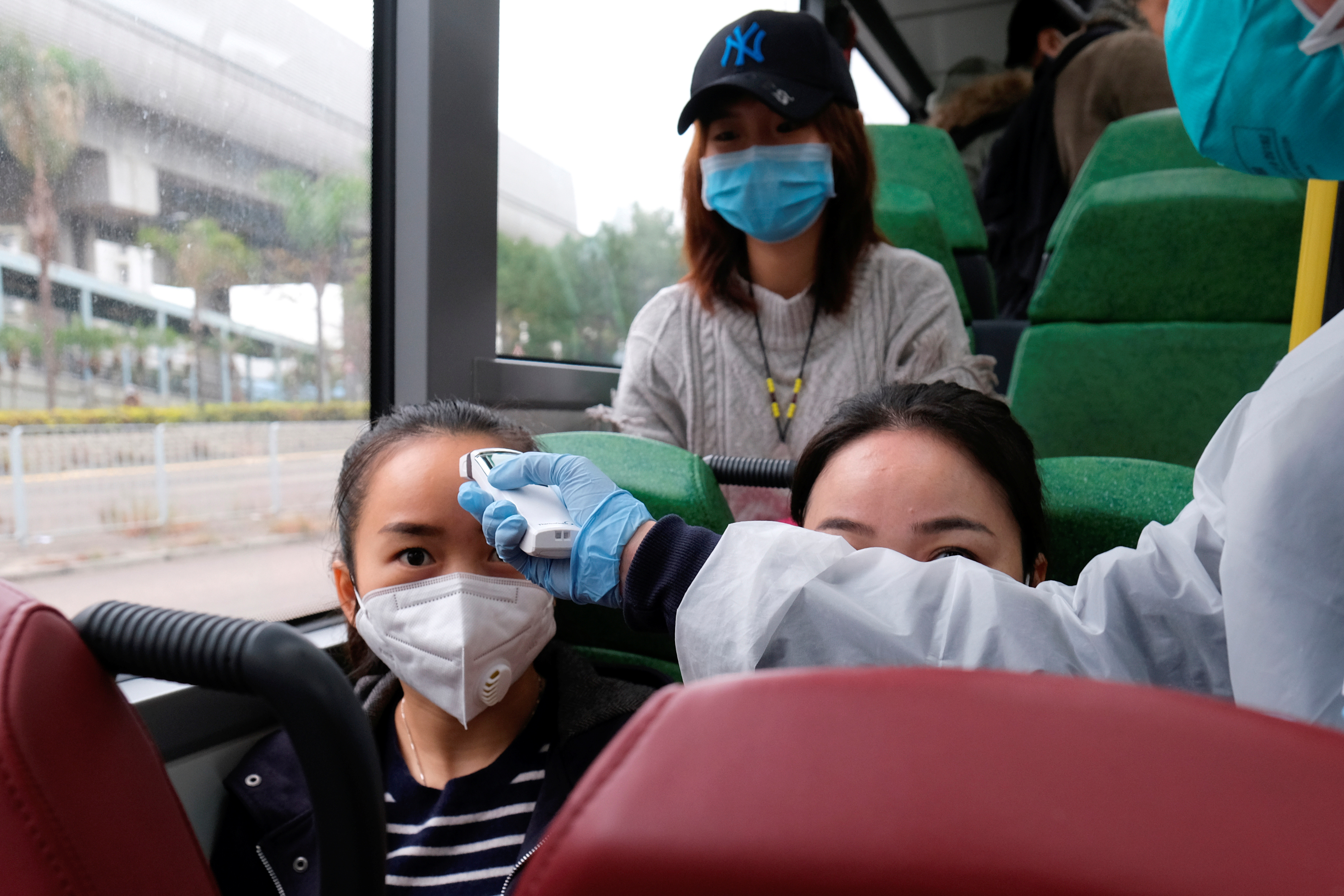 A resident wearing mask and raincoat volunteers to take temperature of passenger following the outbreak of a new coronavirus at a bus stop at Tin Shui Wai, a border town in Hong Kong