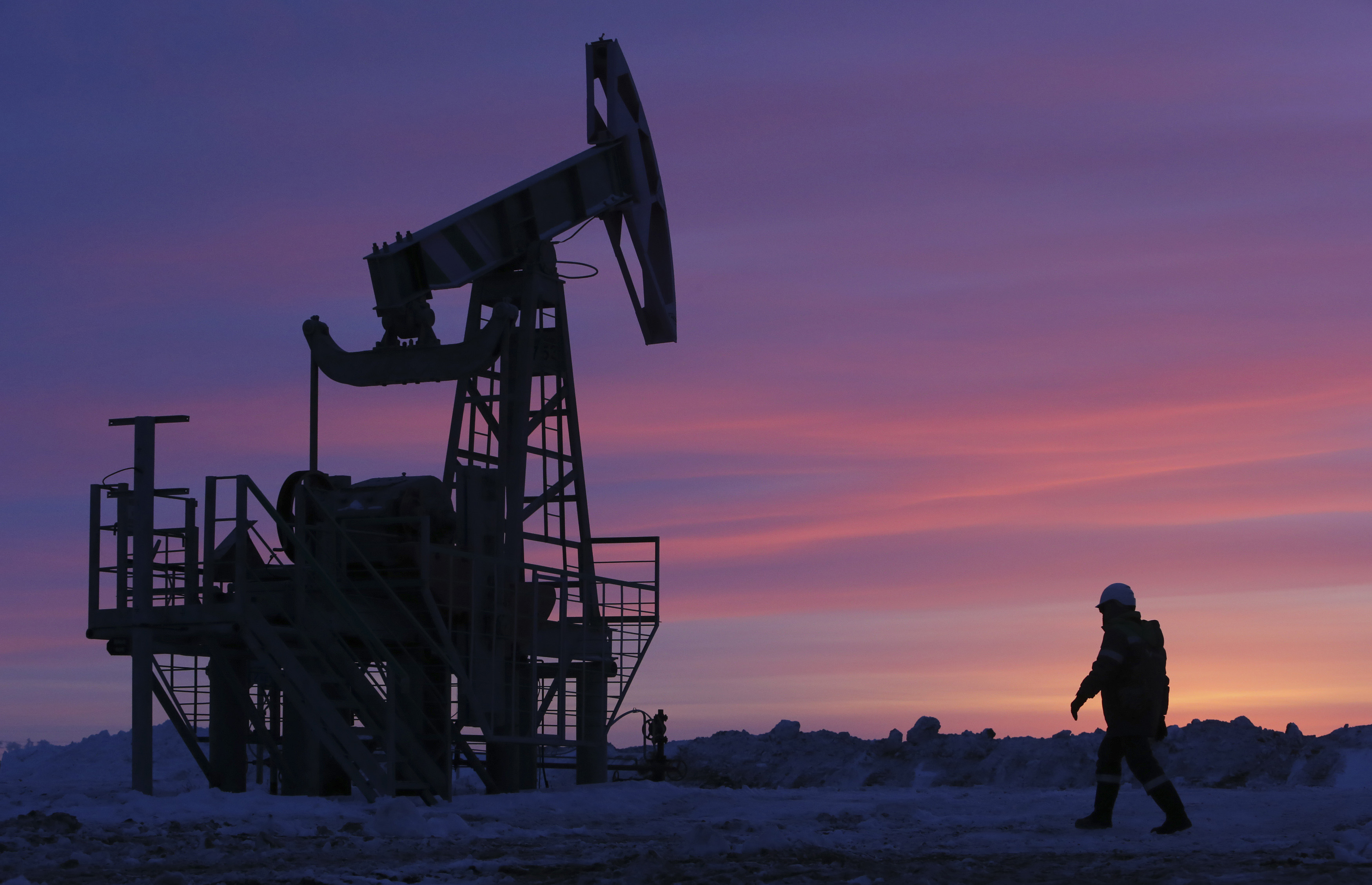 A worker walks past a pump jack on an oil field owned by Bashneft company near Nikolo-Berezovka
