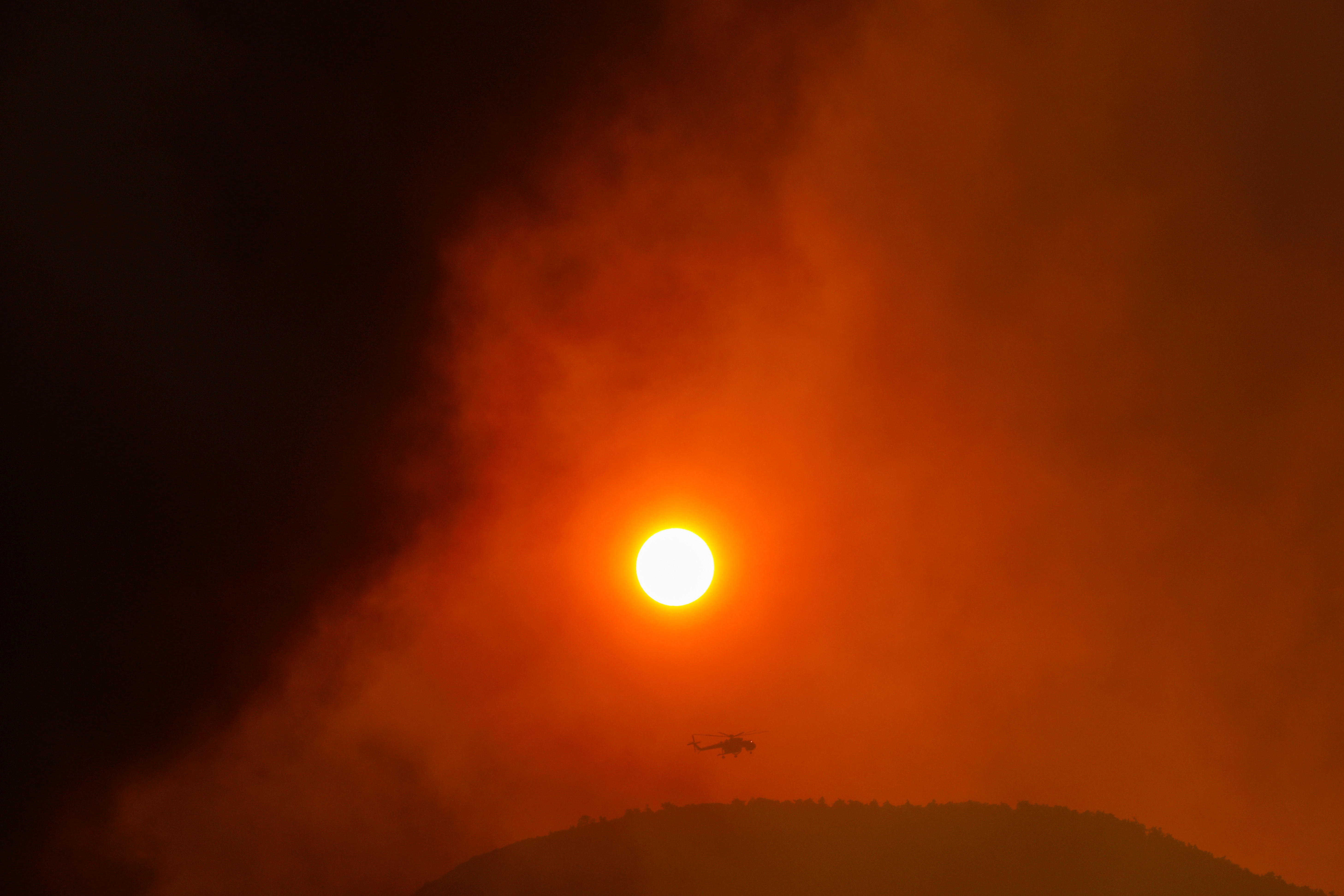 A firefighting helicopter flies by the sun as a wildfire burns in the village of Vilia, Greece, August 18, 2021. REUTERS/Alkis Konstantinidis