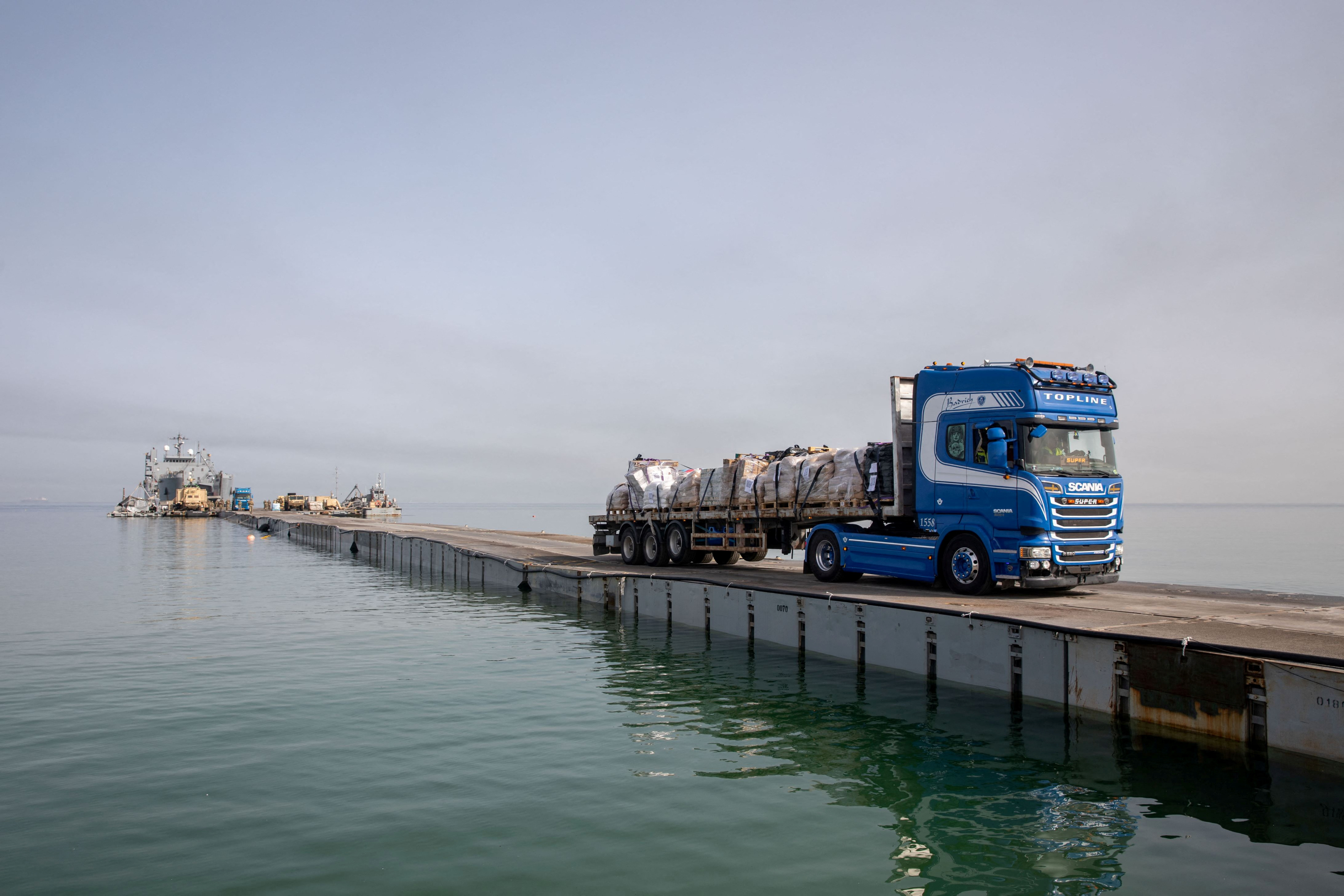Trucks deliver humanitarian aid over a temporary pier on the Gaza coast