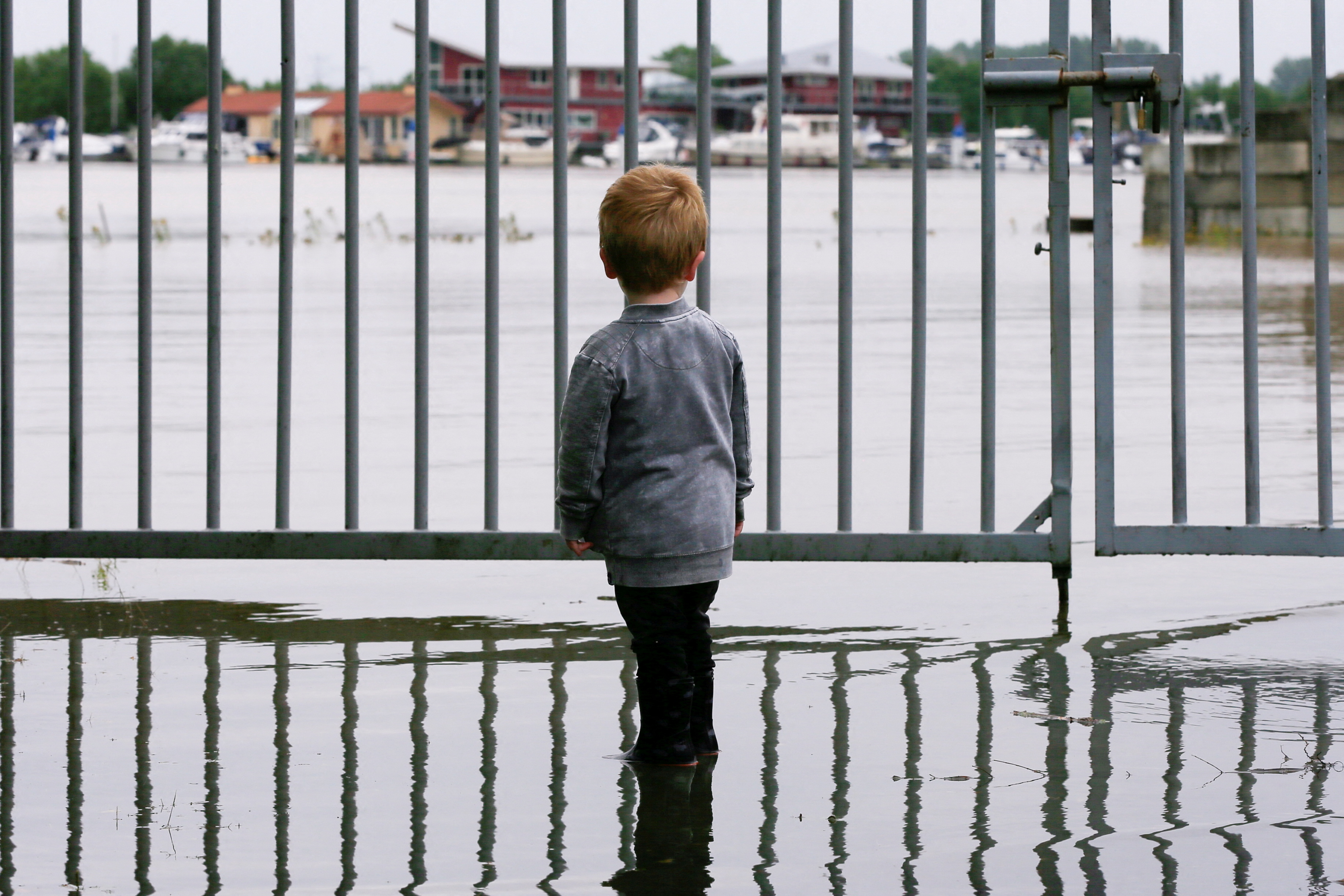 A child looks on as water floods through a fence, in Wessem
