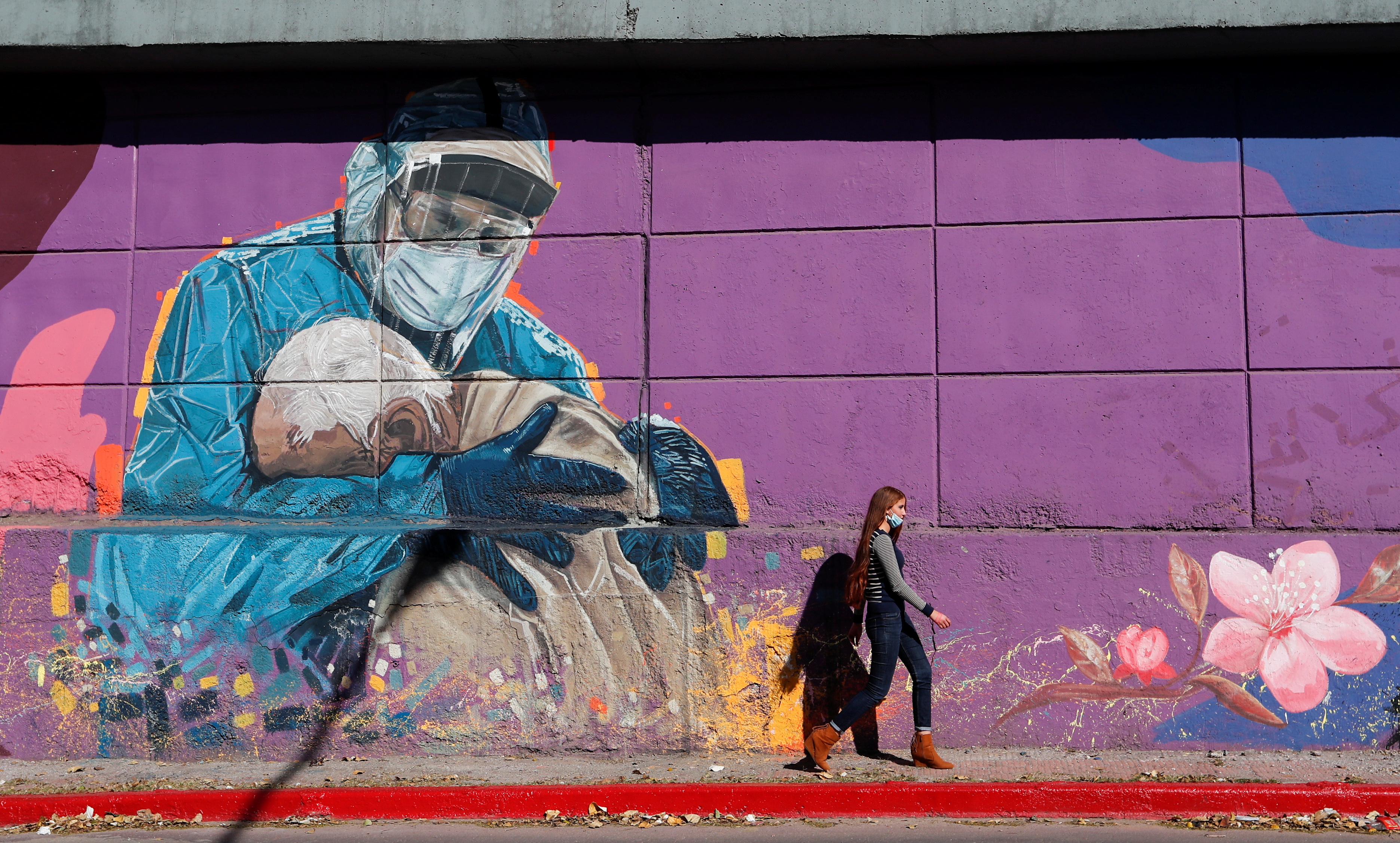 A woman walks past a graffitti depicting a healthcare worker embracing a man, during the coronavirus disease (COVID-19) pandemic, in Cordoba, Argentina, July 10, 2021. Picture taken July 10, 2021. REUTERS/Agustin Marcarian