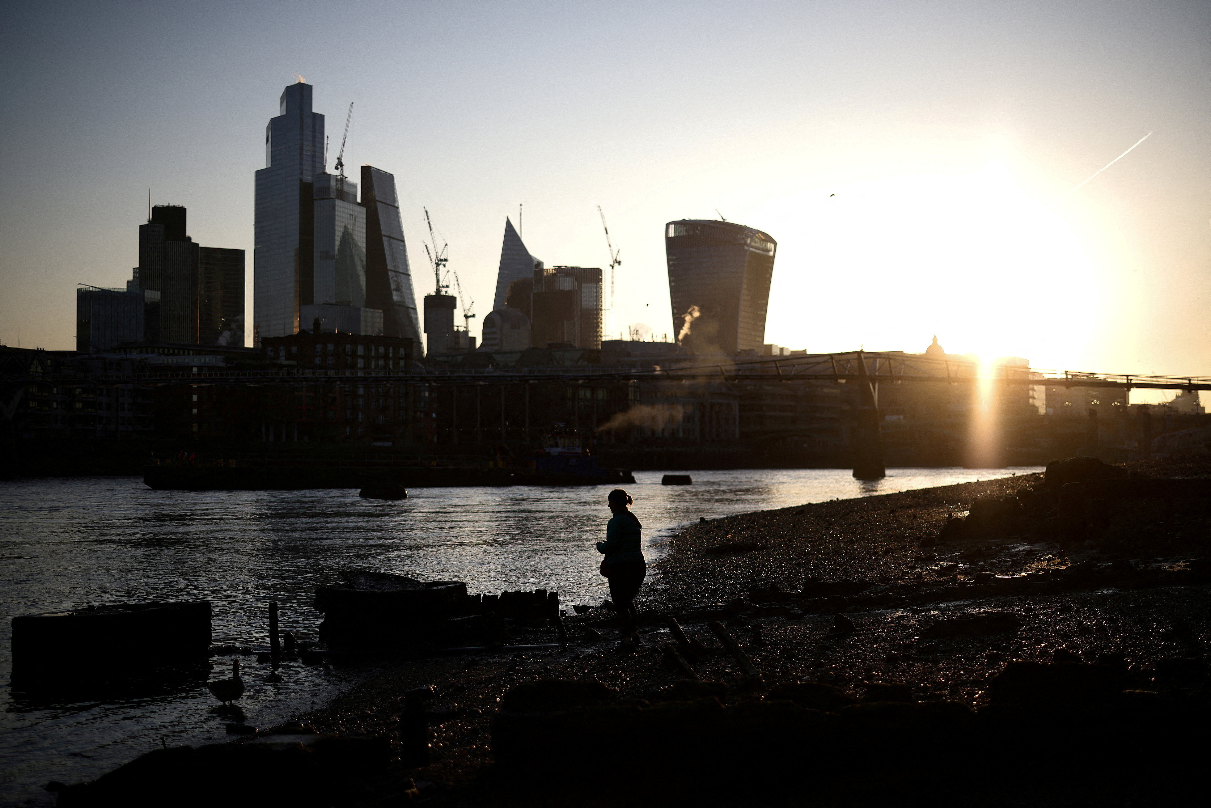 A person stands on the bank of the River Thames during sunrise in London