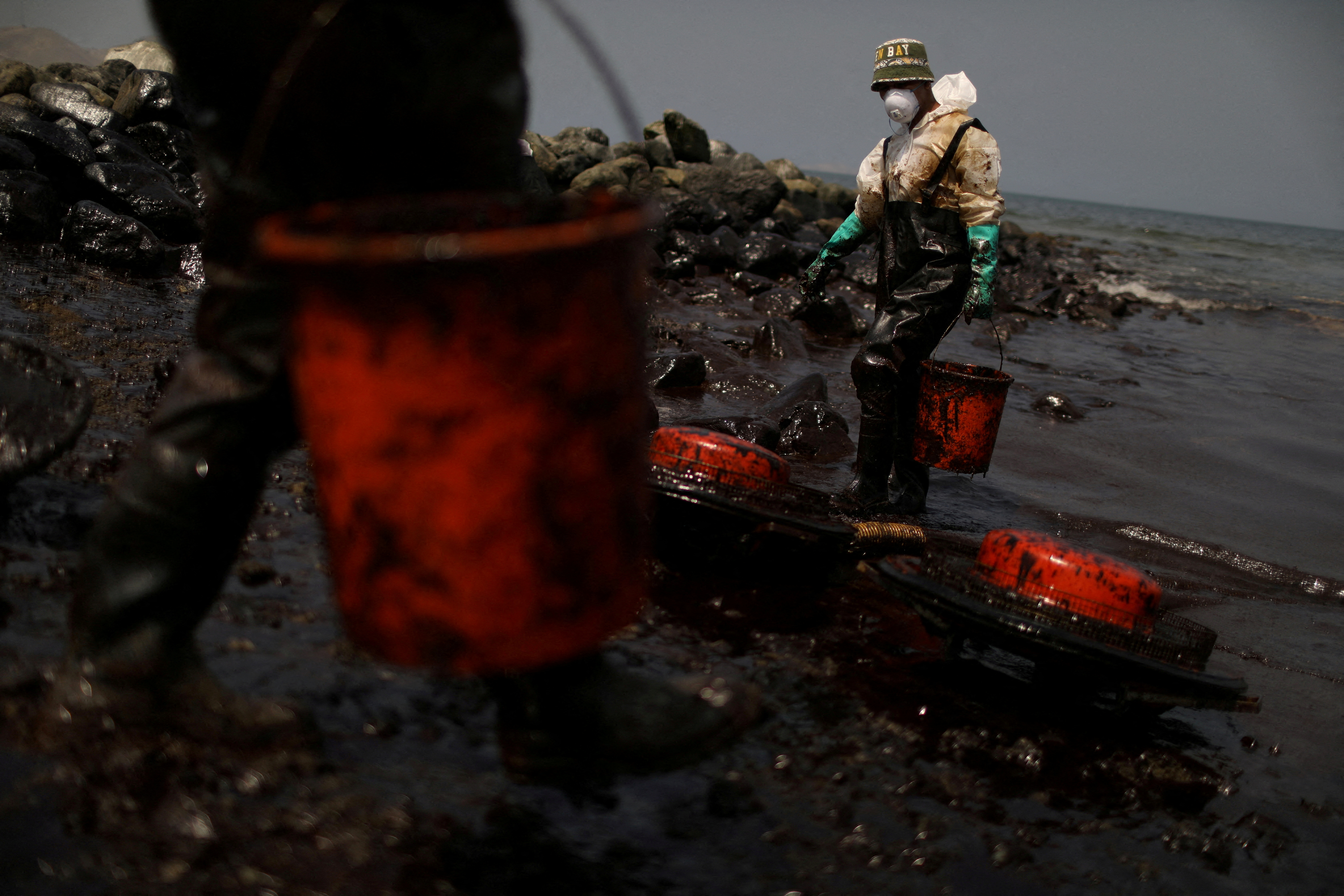 Workers clean up an oil spill following an underwater volcanic eruption, in Ancon