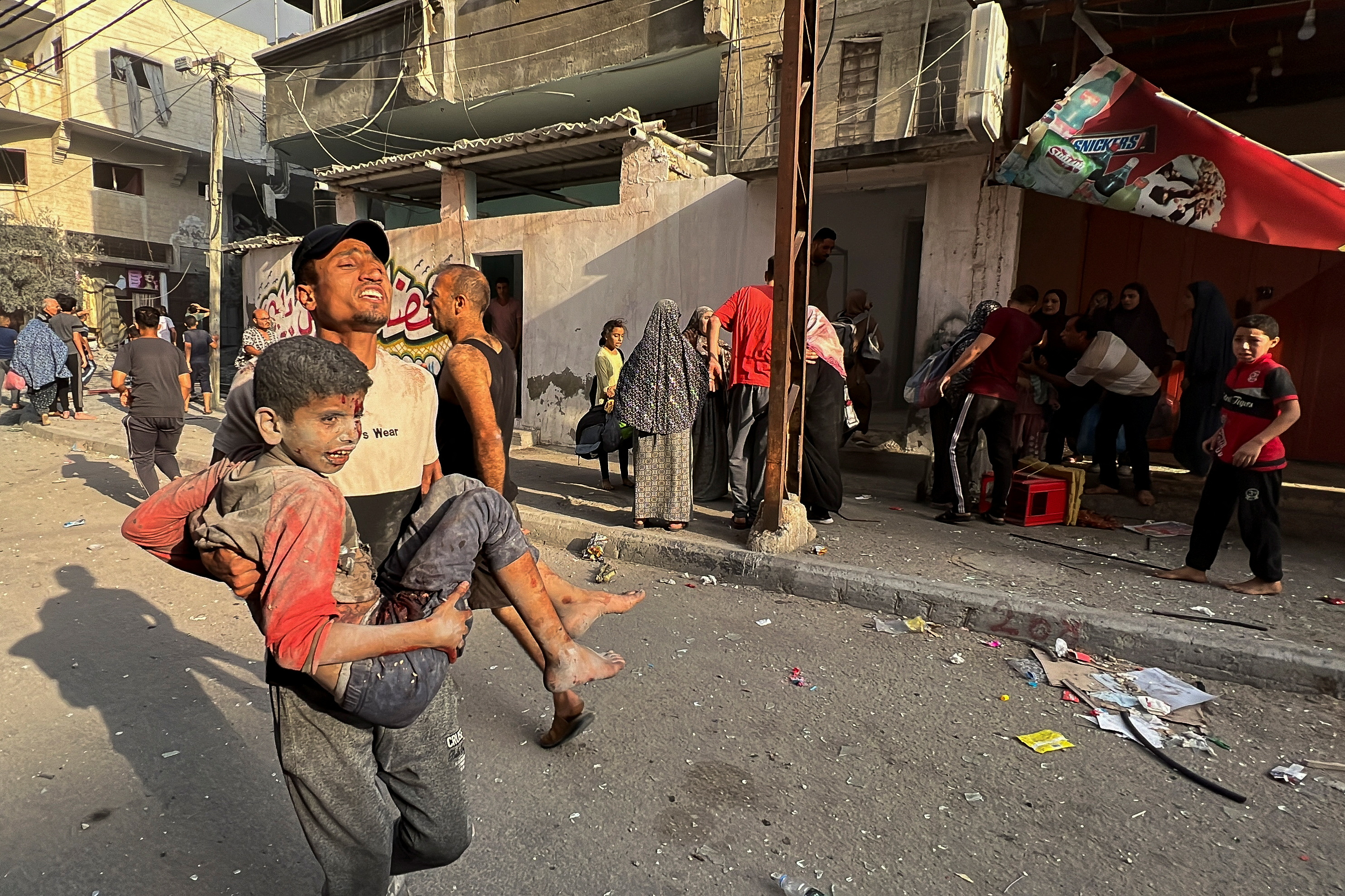 A Palestinian carries a child casualty at the site of Israeli strikes on houses, in Gaza City