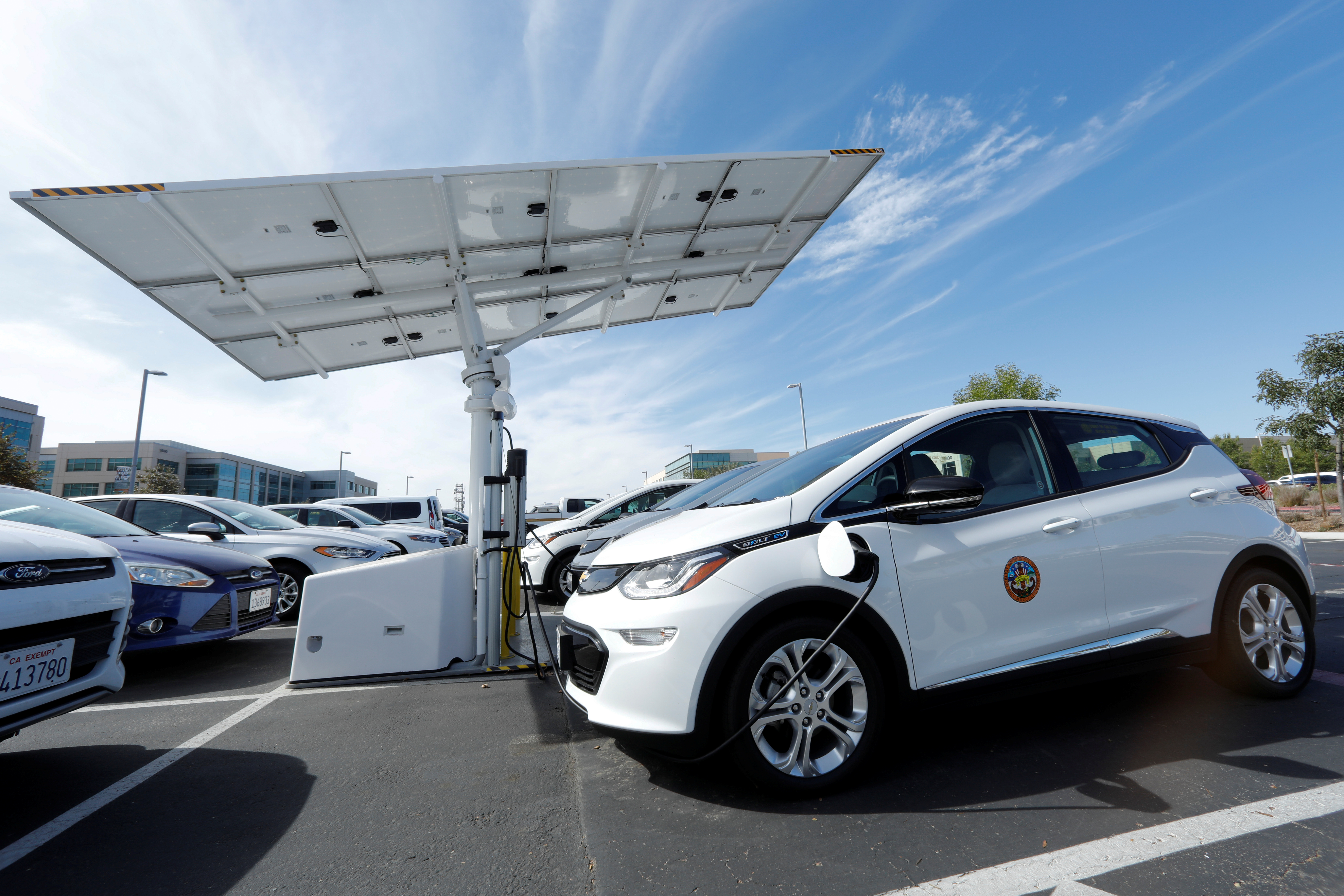 A small fleet of electric Chevrolet Bolt vehicles are charged by a sun tracking  solar panel car charing system in San Diego