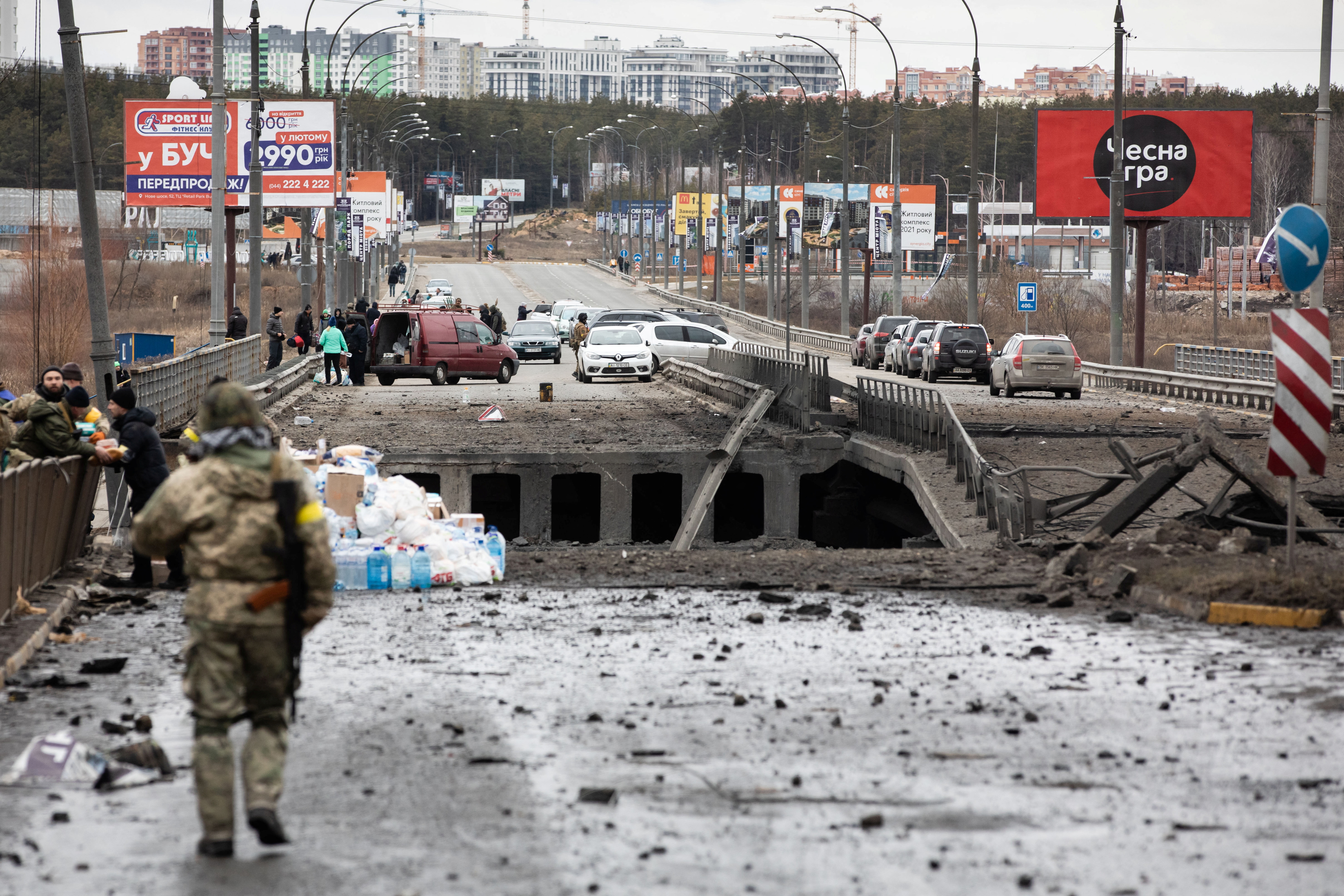 Evacuees fleeing Ukraine-Russia conflict cross a destroyed bridge in the Kyiv region