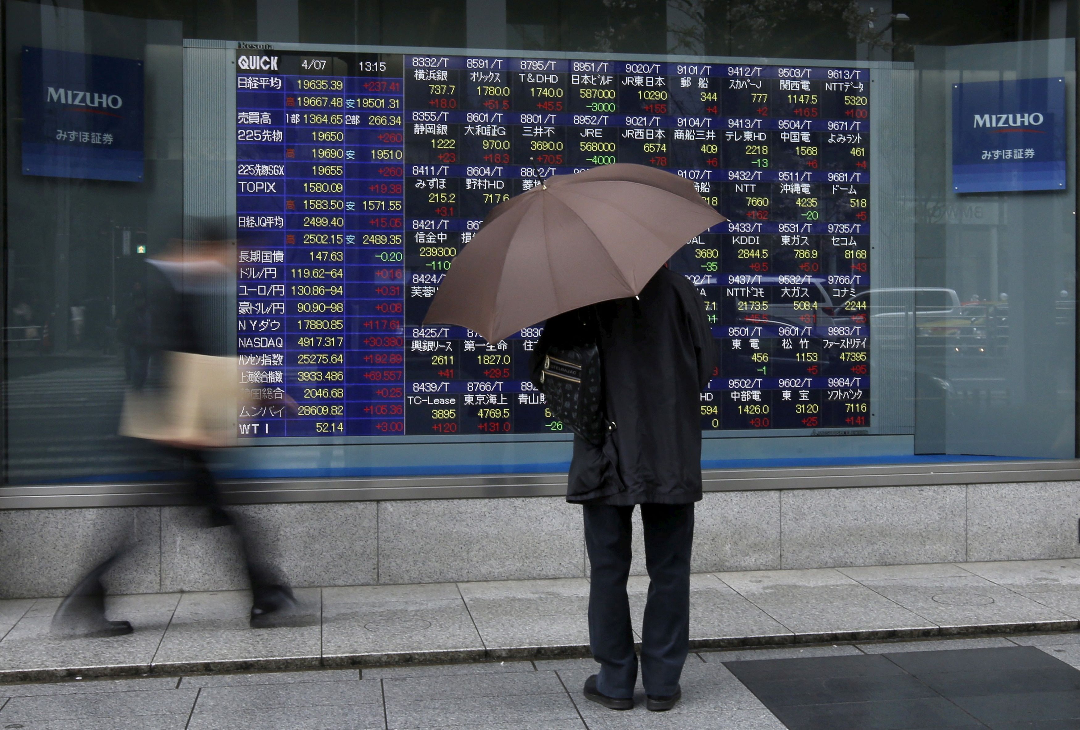 A man holding an umbrella looks at an electronic stock quotation board outside a brokerage in Tokyo