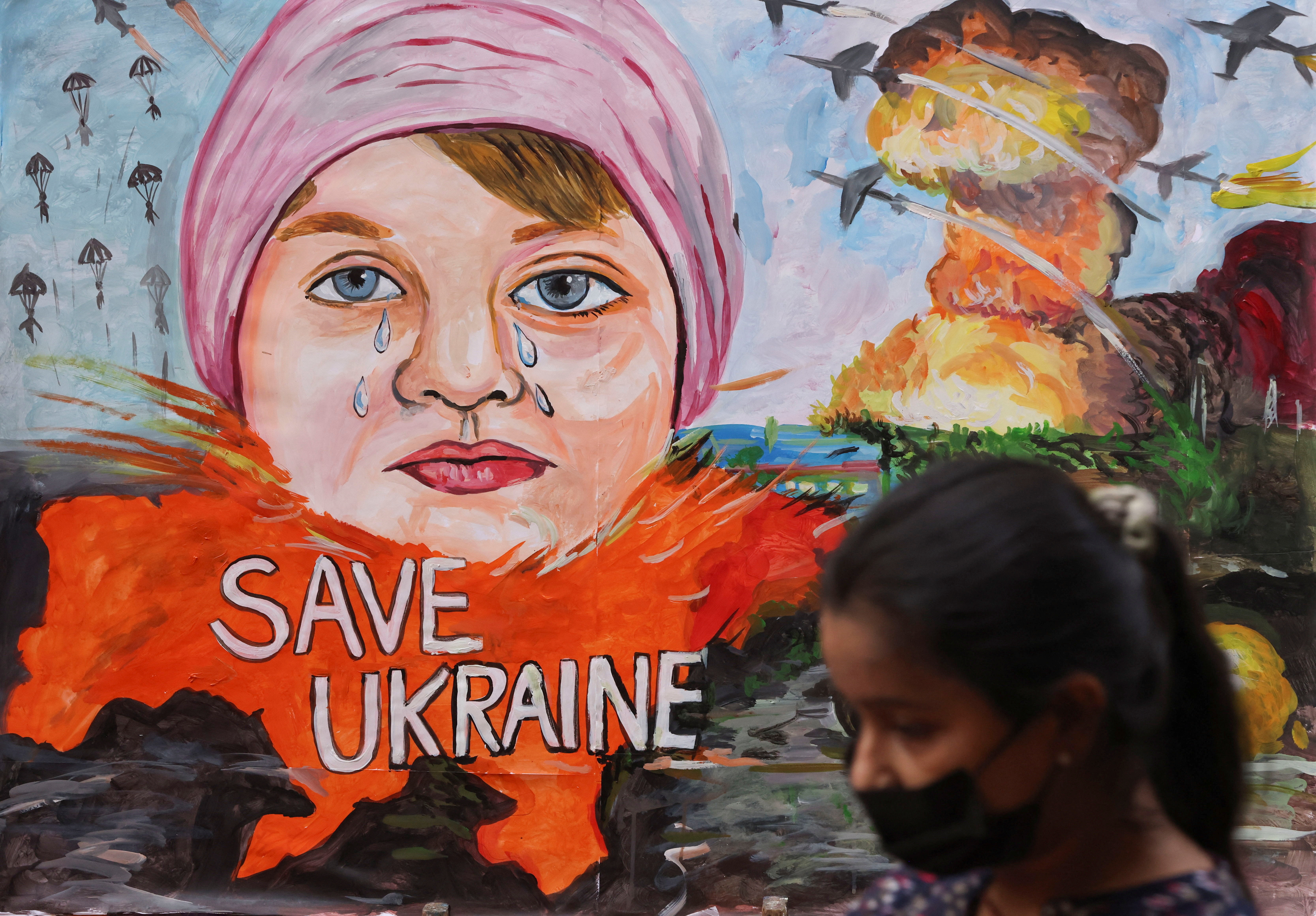 A girl walks past a painting depicting the crisis between Russia and Ukraine, outside an art school in Mumbai
