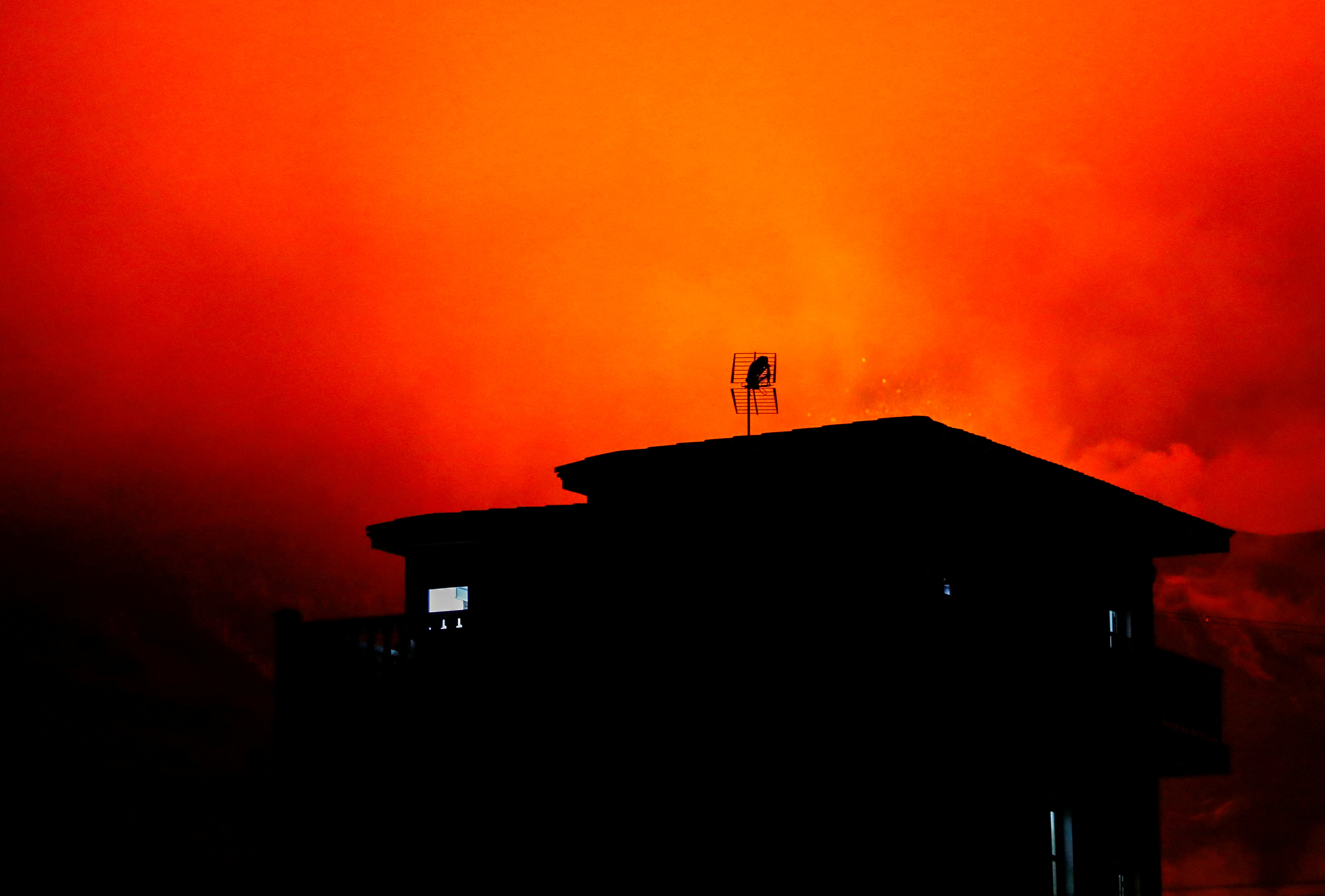 A house in Tajuya is seen with the Cumbre Vieja volcano behind expelling lava and ash