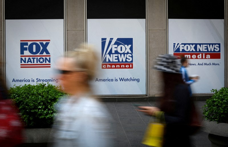 People walk past Fox News posters on News Corporation and Fox News headquarters building in New York City