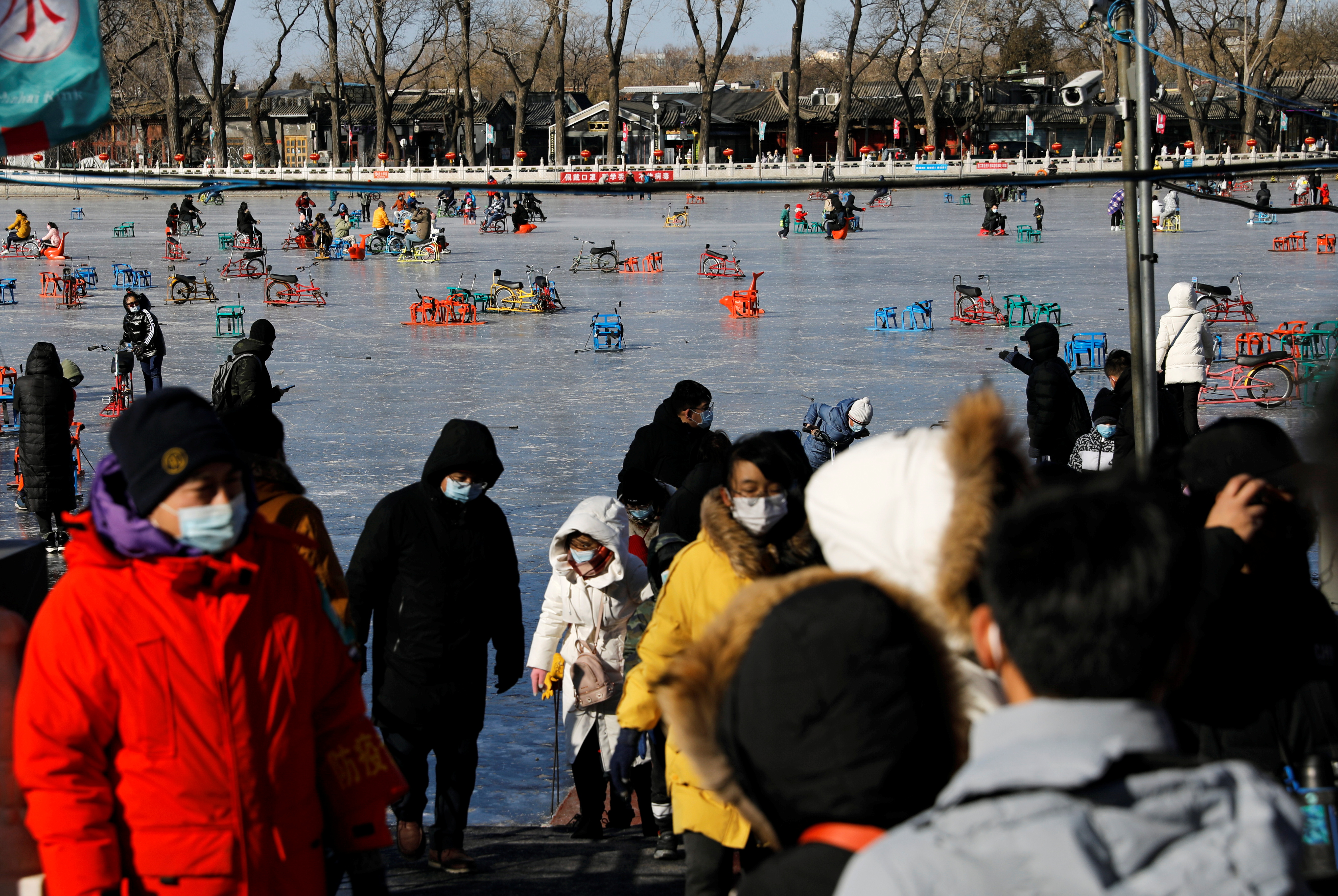 People wearing face masks stand at the entrance of a frozen lake which has been turned to an ice rink, following the coronavirus disease (COVID-19) outbreak, in Beijing, China January 16, 2021. REUTERS/Tingshu Wang