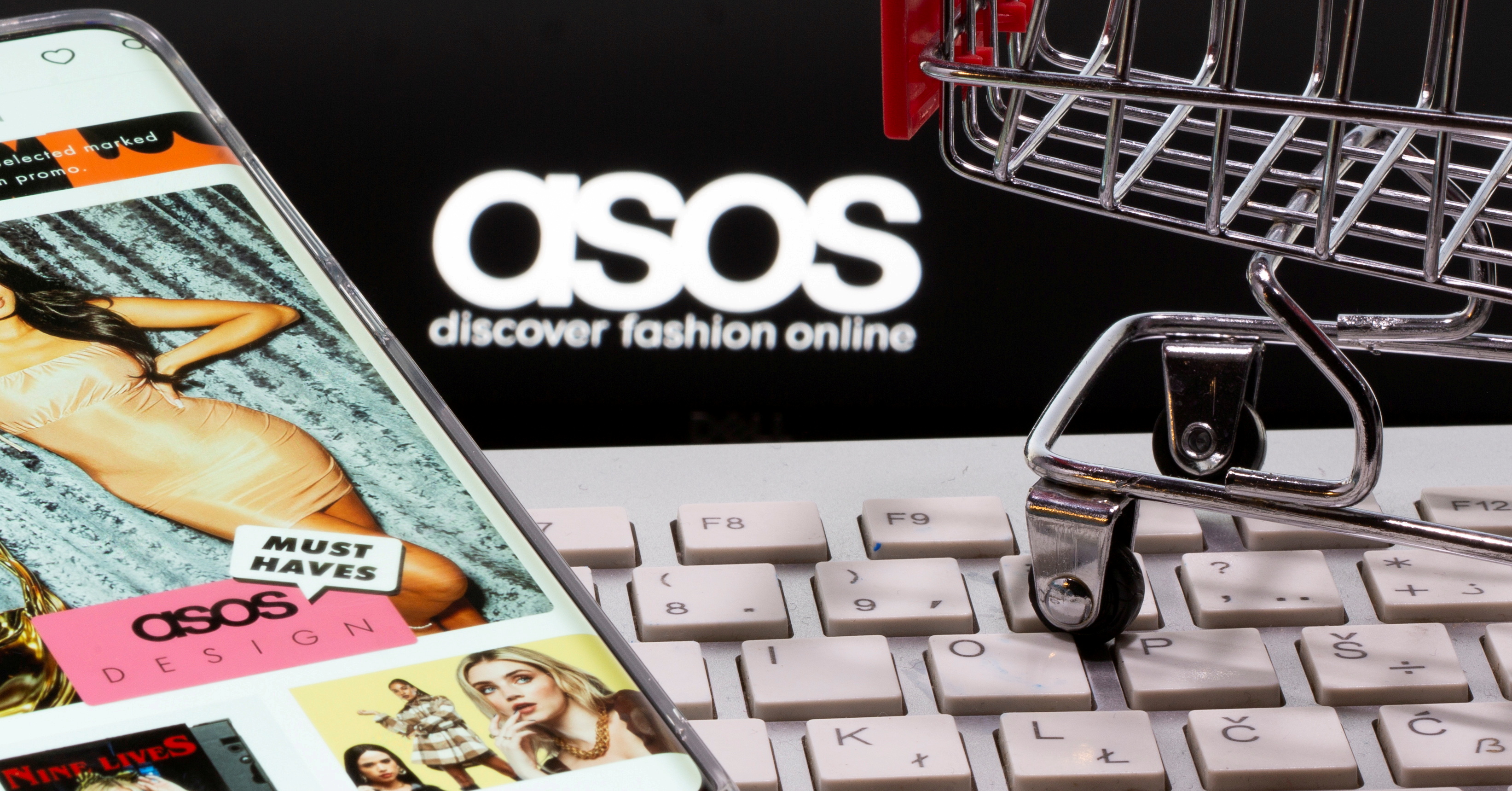 FILE PHOTO: A smartphone with the ASOS app and a keyboard and shopping cart are seen in front of a displayed ASOS logo in this illustration picture