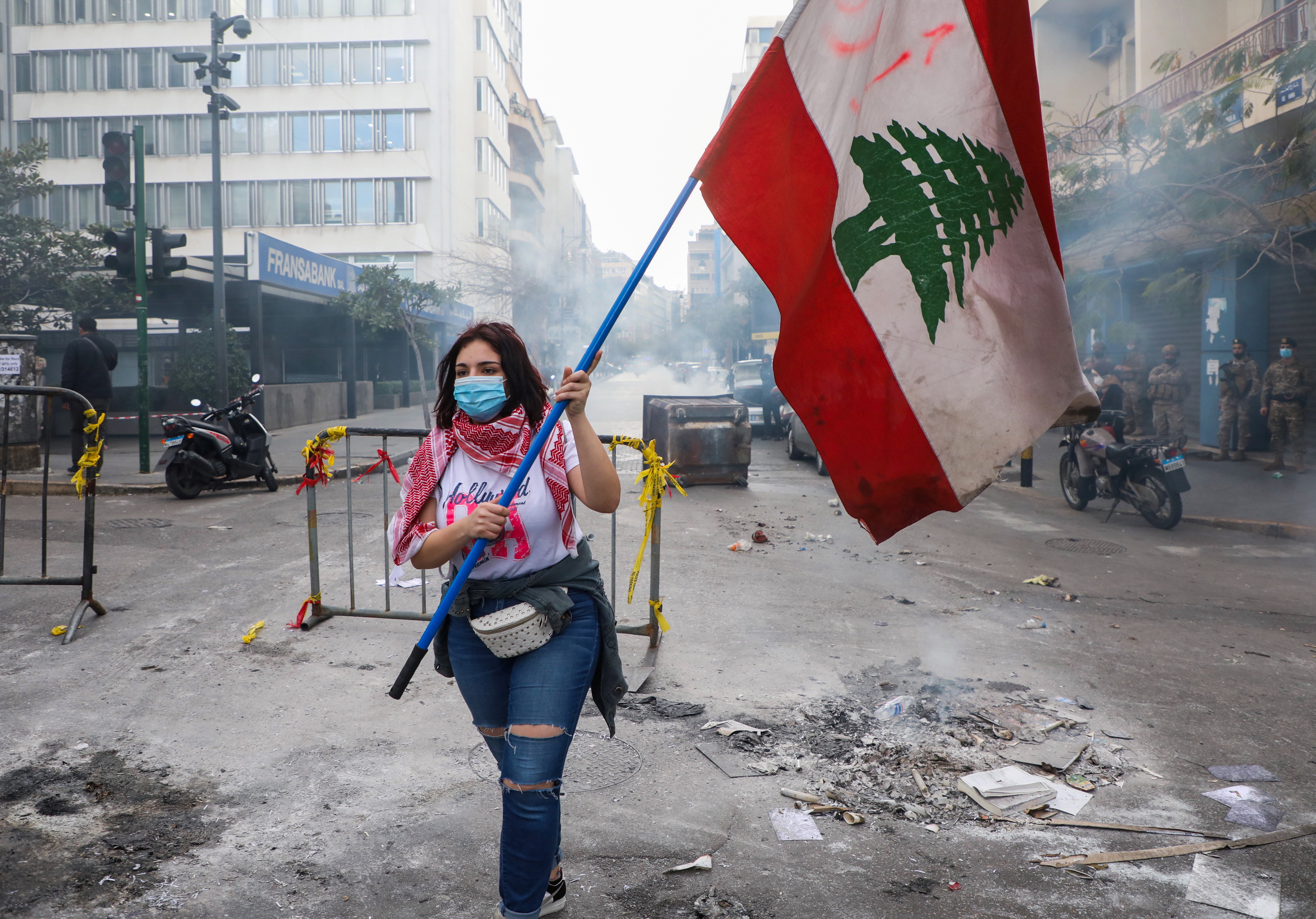 A demonstrator carries a national flag along a blocked road, during a protest against the fall in Lebanese pound currency and mounting economic hardships, near the Central Bank building, in Beirut, Lebanon March 16, 2021. REUTERS/Mohamed Azakir