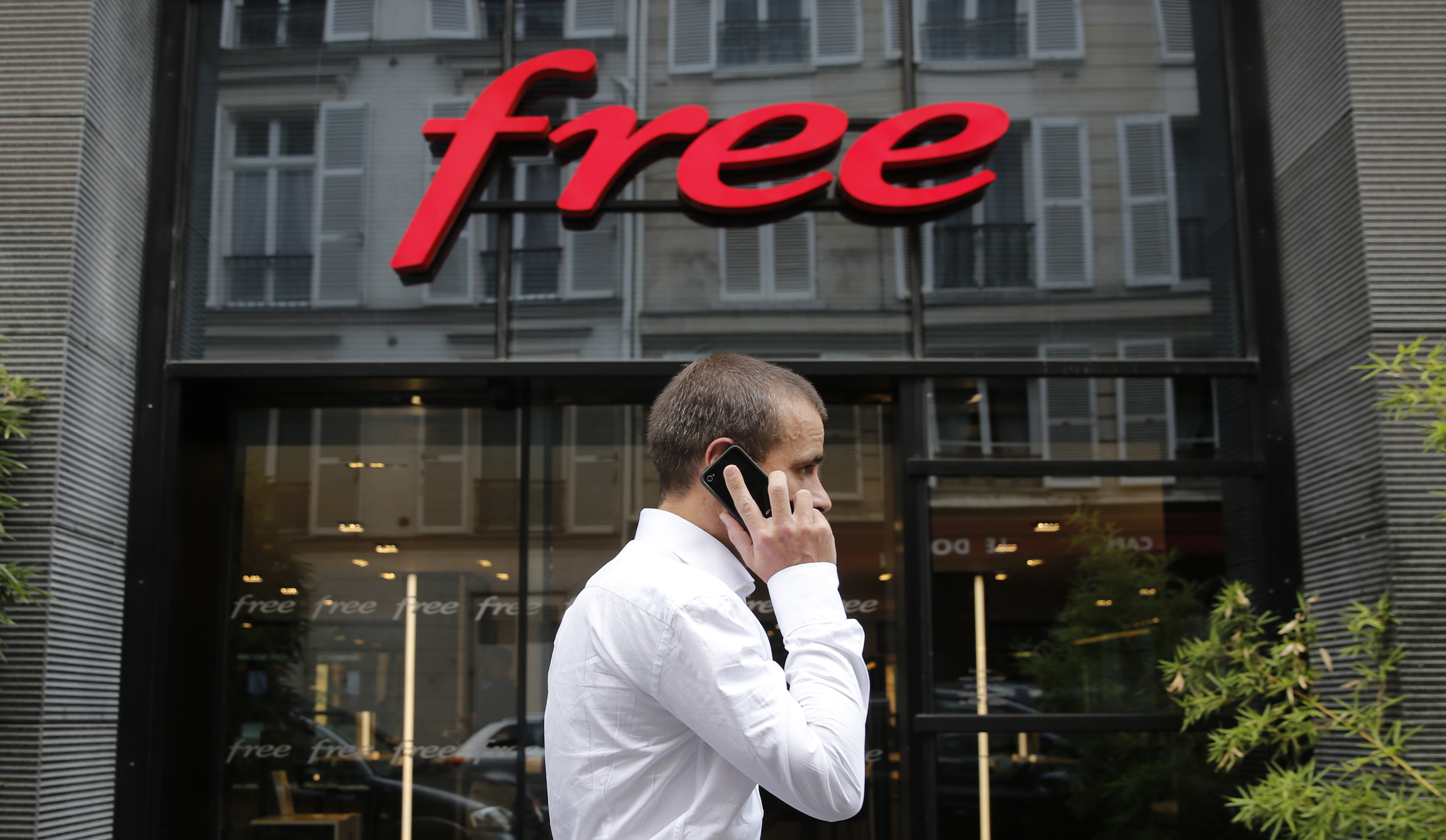 A man uses his mobile phone as he walks pas the main entrance of French internet service provider and mobile phone operator Free at the company headquarters in Paris