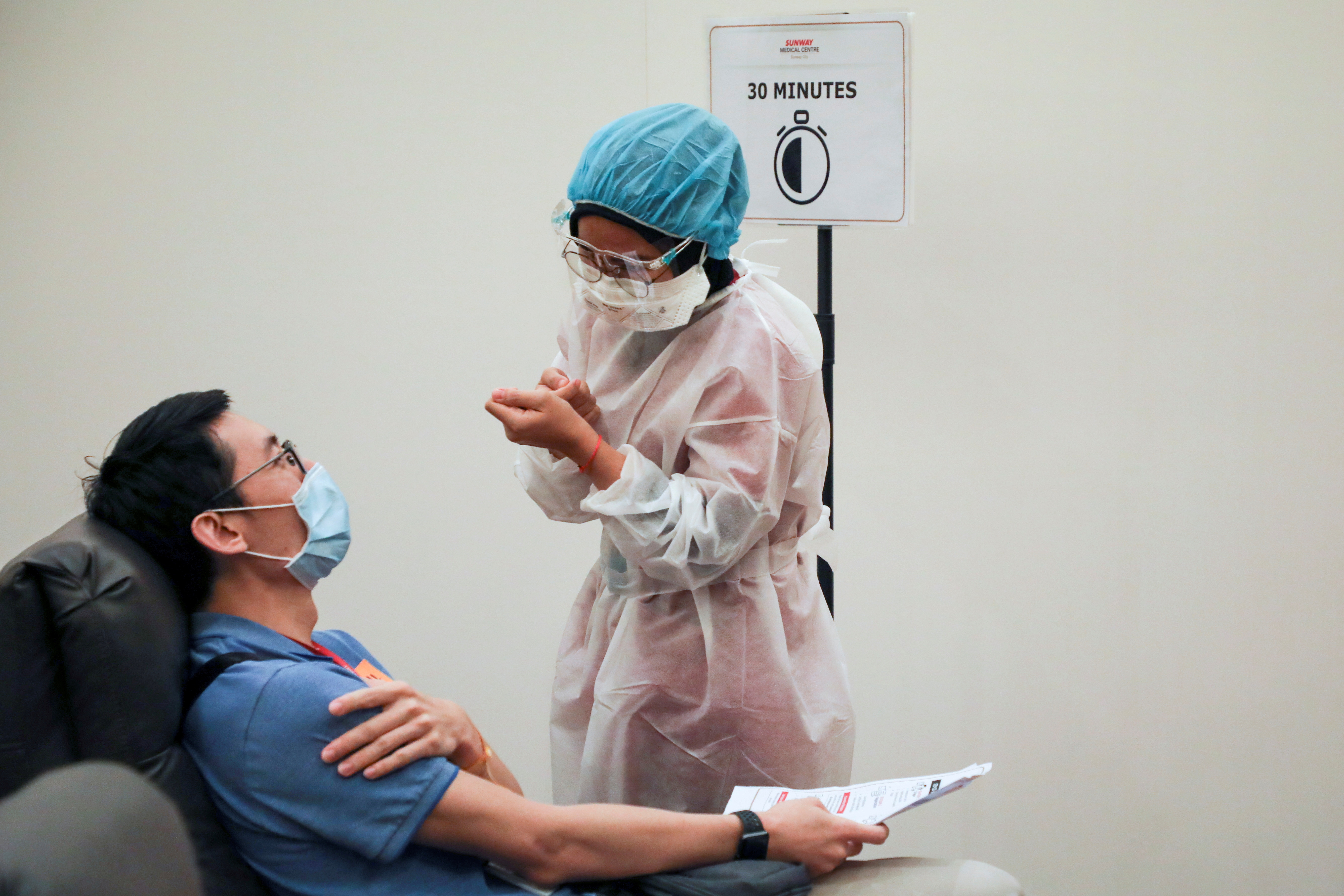 2021 年 3 月 12 日，在马来西亚梳邦再也的双威医疗中心，一名医务人员在接受冠状病毒病（COVID-19）疫苗后与一名接受观察的男子交谈。REUTERS/Lim Huey Teng/文件照片