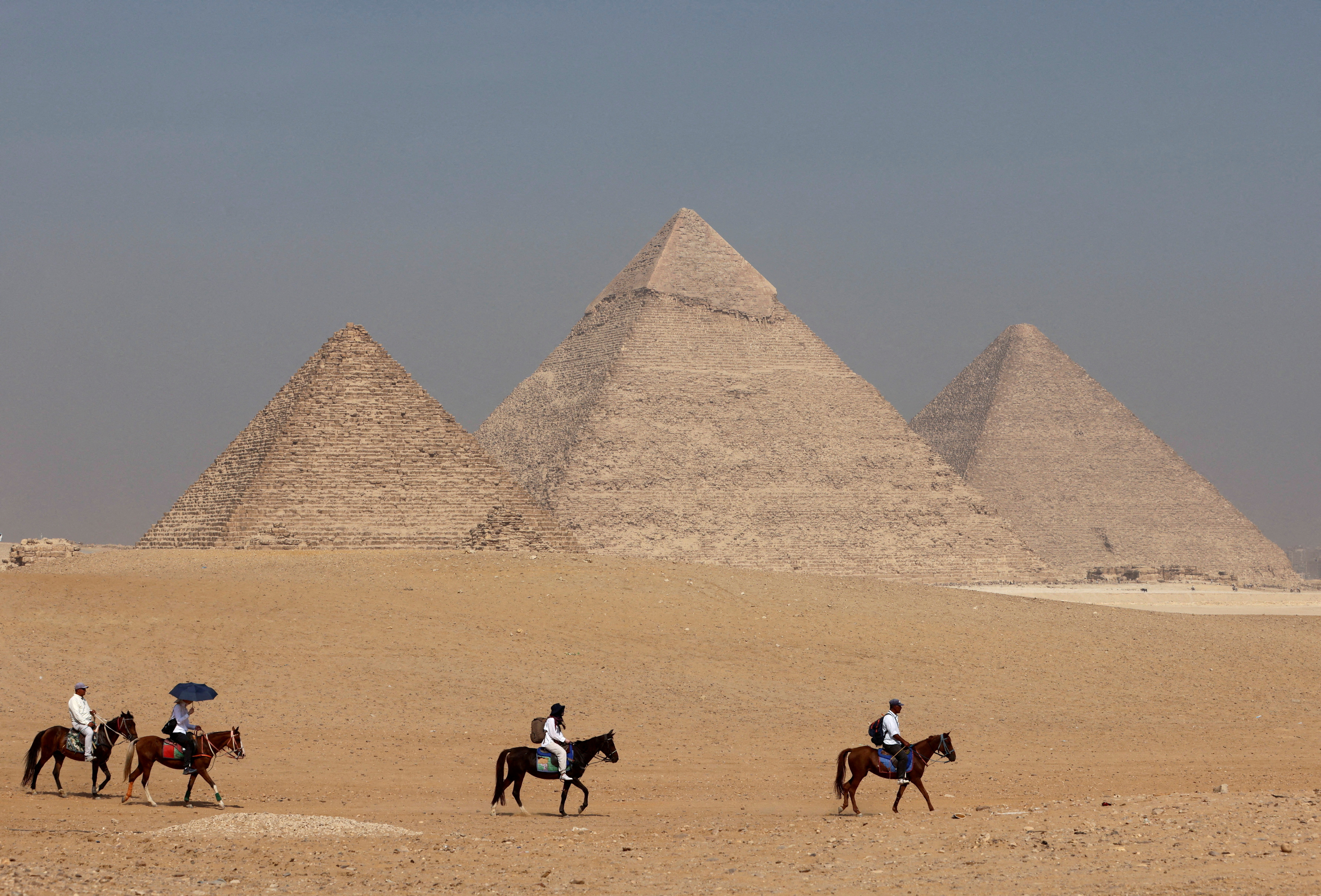 Tourists ride horses in front of the Great Pyramid of Giza